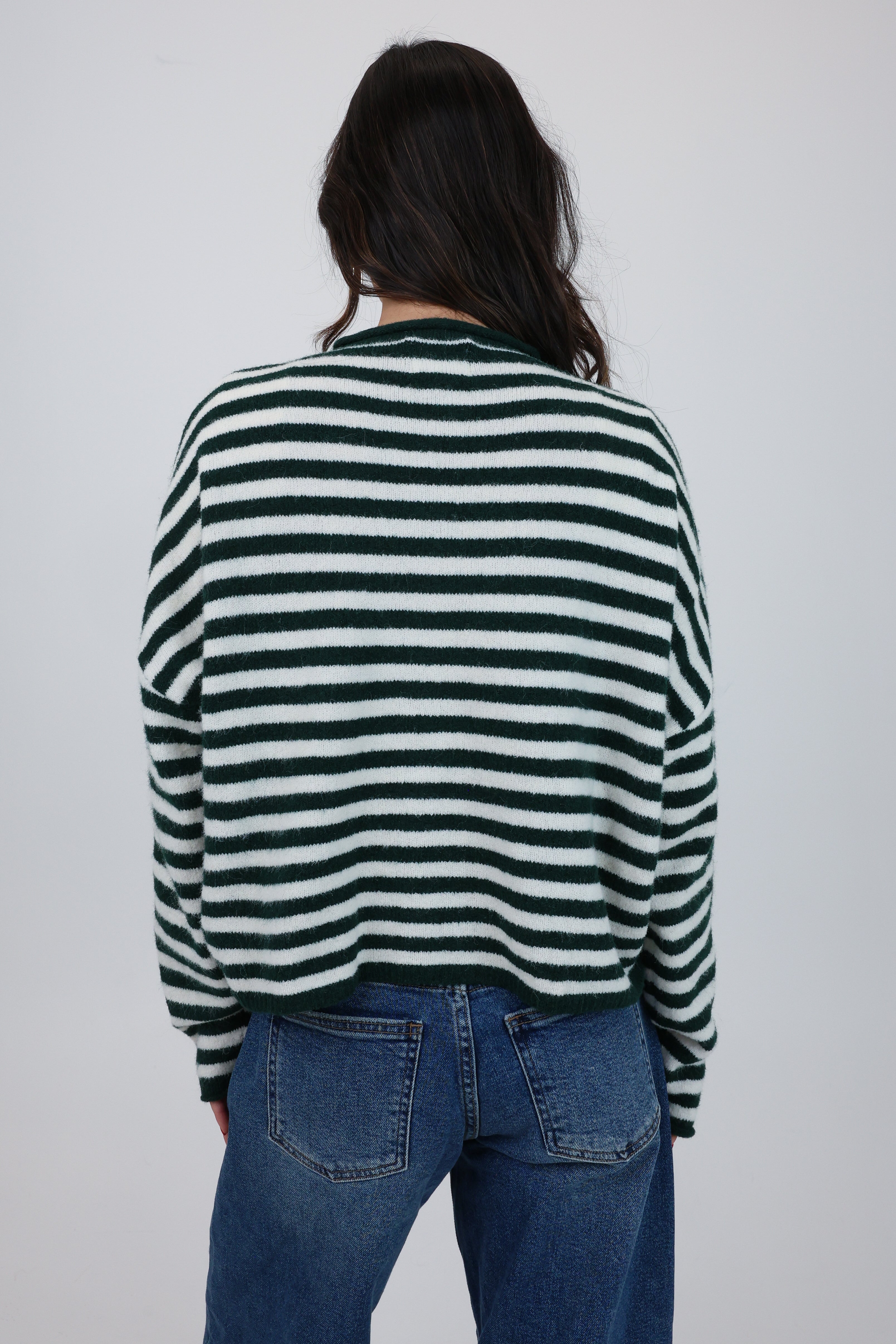 Person wearing a green and white striped sweater and blue jeans on a plain background