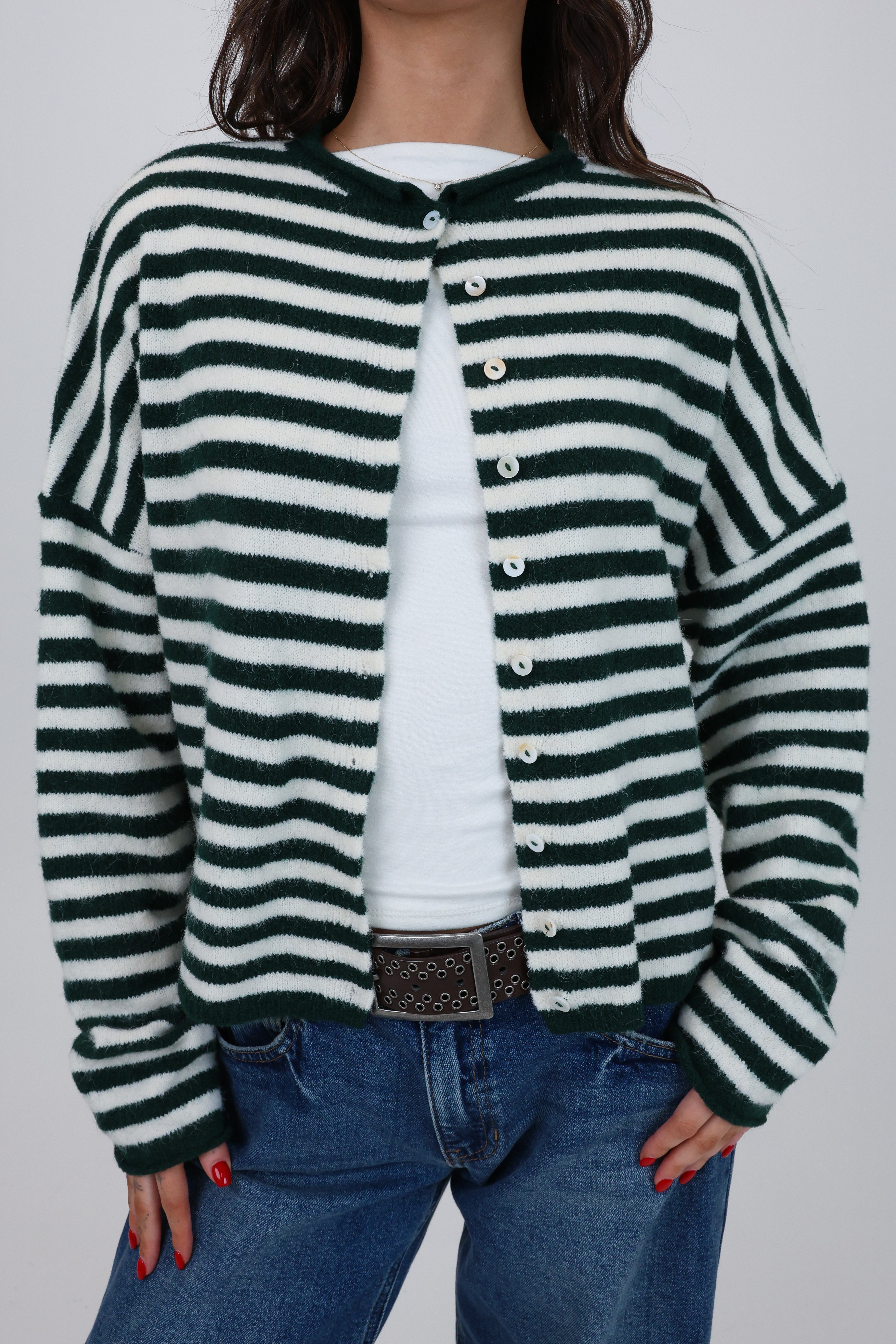 Person wearing a green and white striped cardigan over a white shirt with blue jeans on a plain background