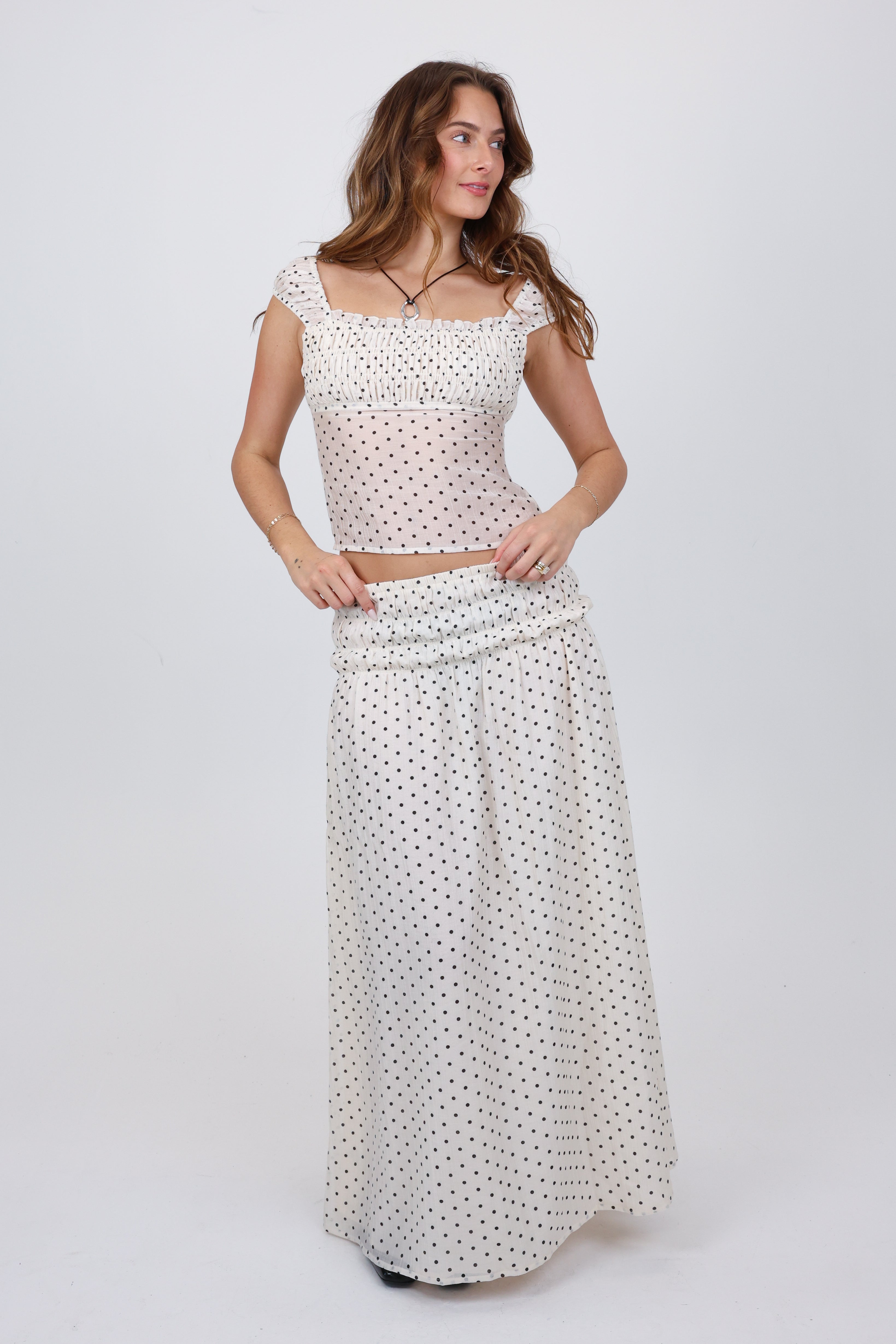 Woman wearing a white polka dot top and long skirt on a white background