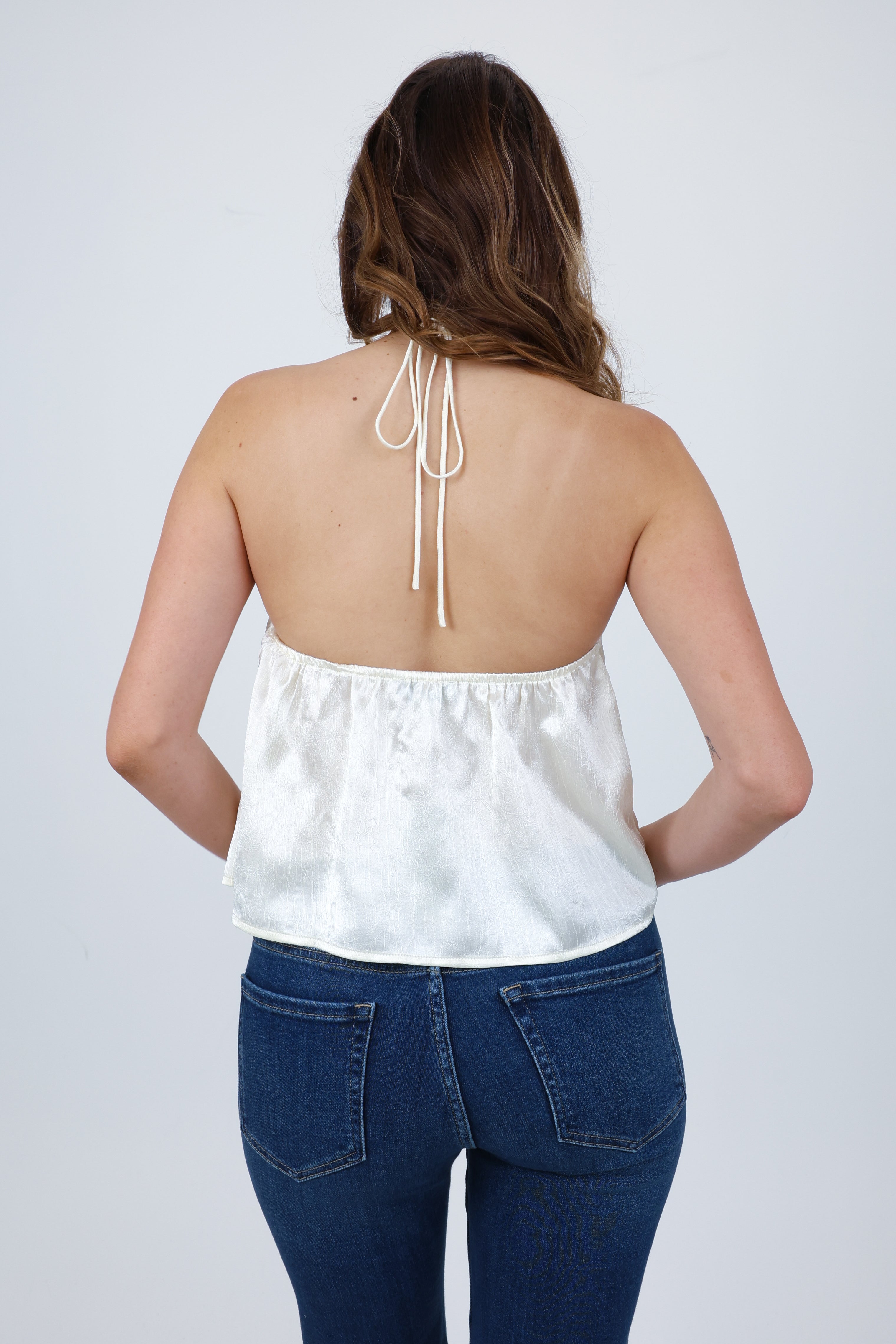 Person wearing a white strapless top and blue jeans on a plain background