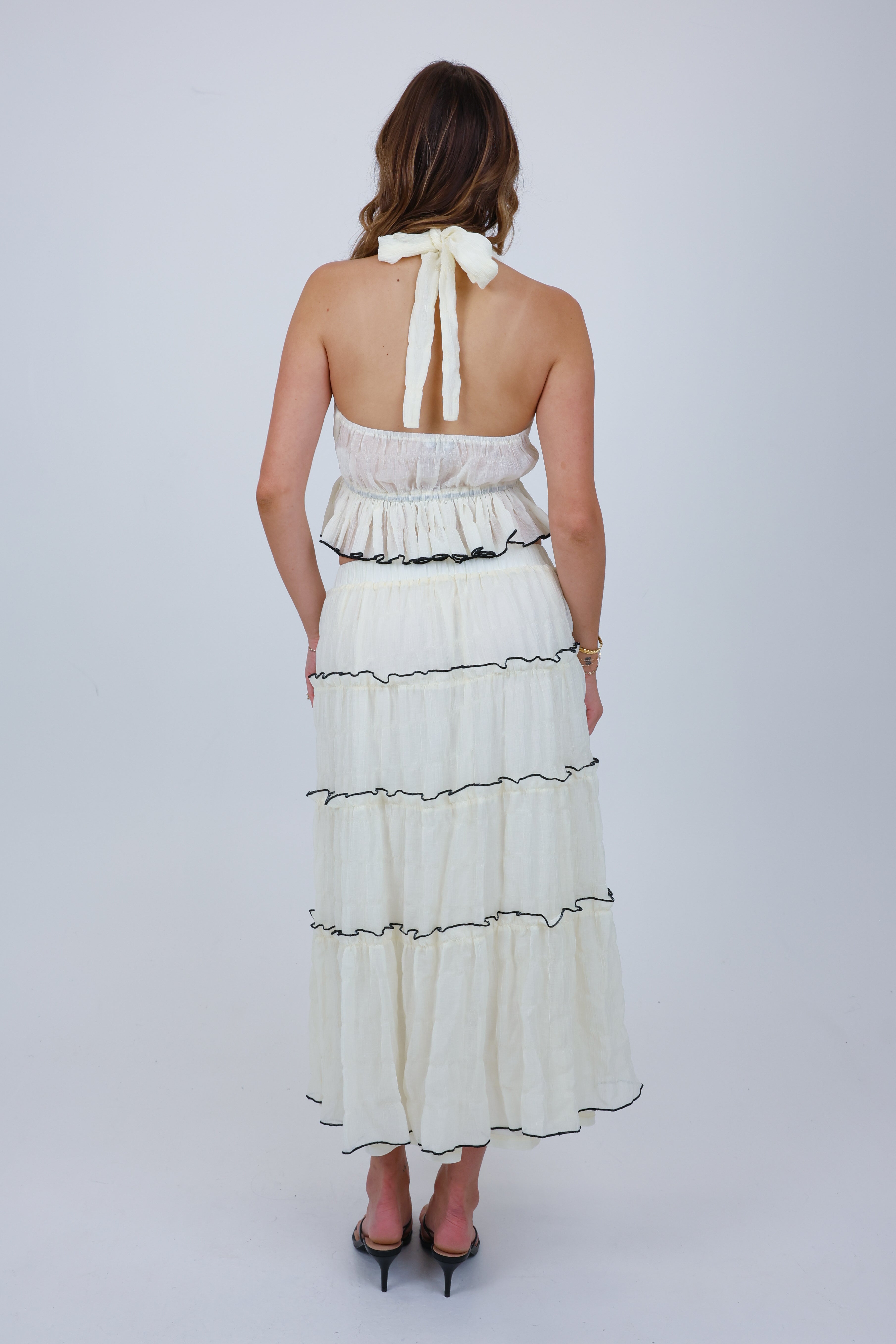 Woman wearing a white halter neck dress with ruffled layers on a plain background