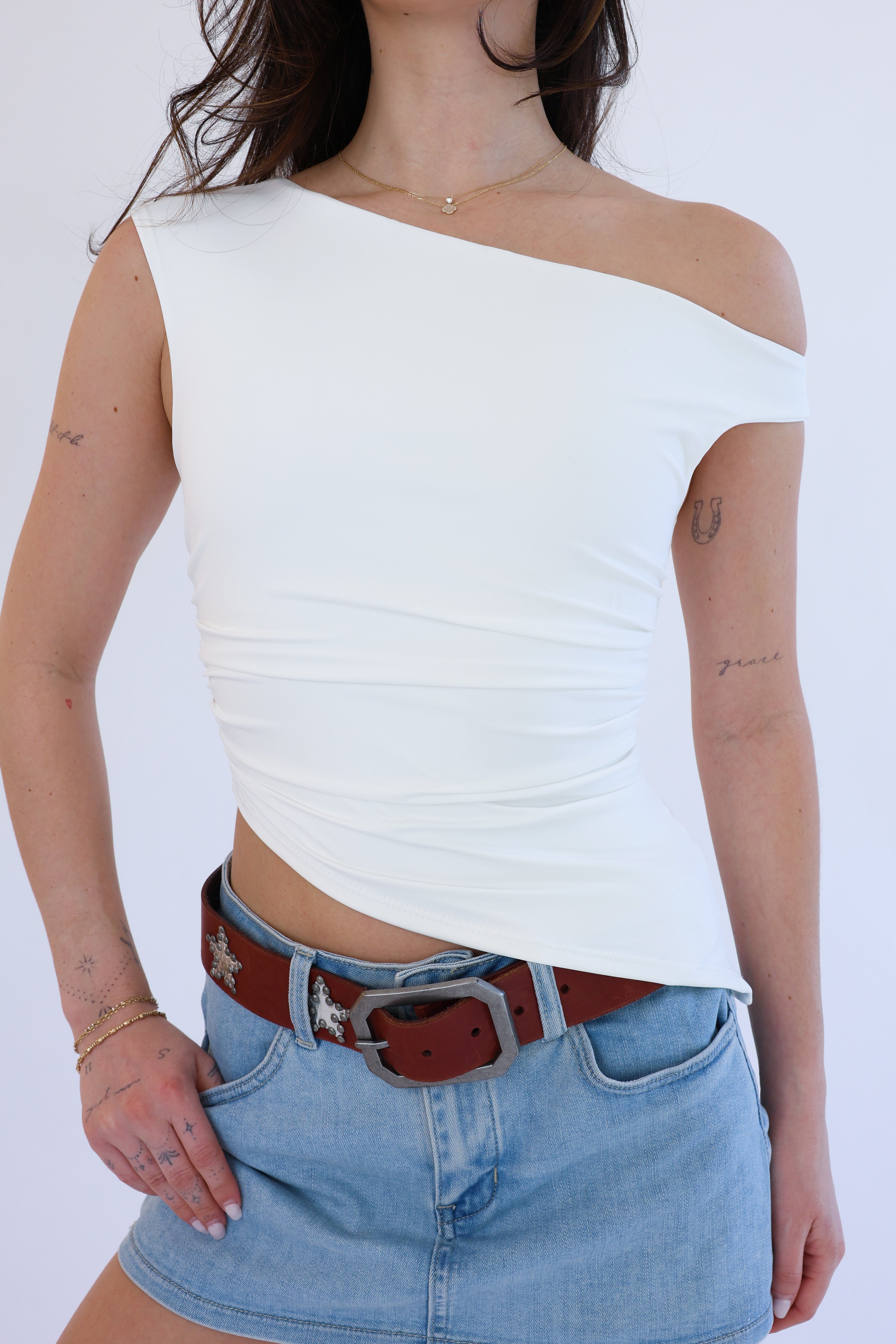 Person wearing a white off-shoulder top and blue jeans with a brown belt on a white background