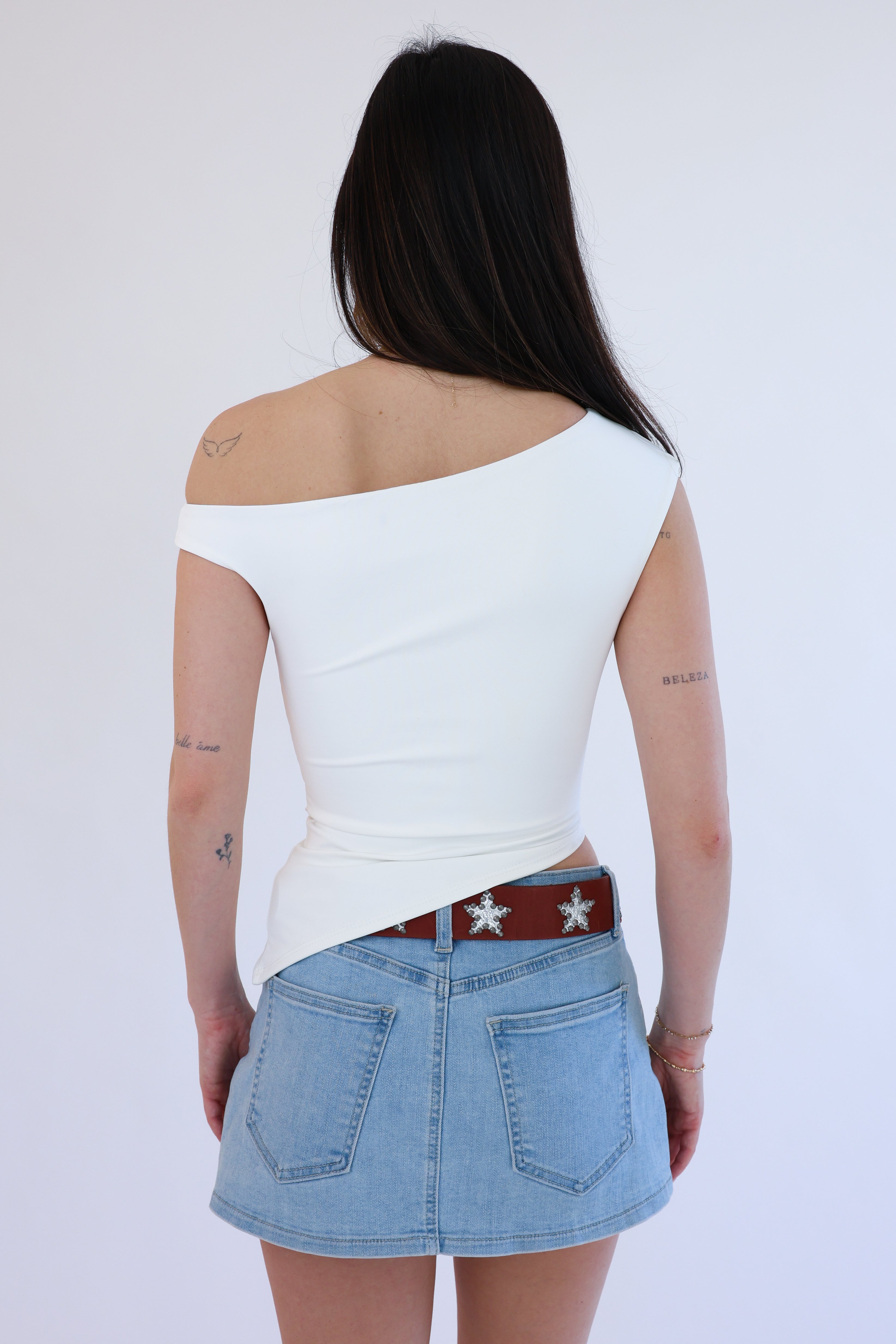Person wearing a white top and denim skirt with a red belt on a plain background