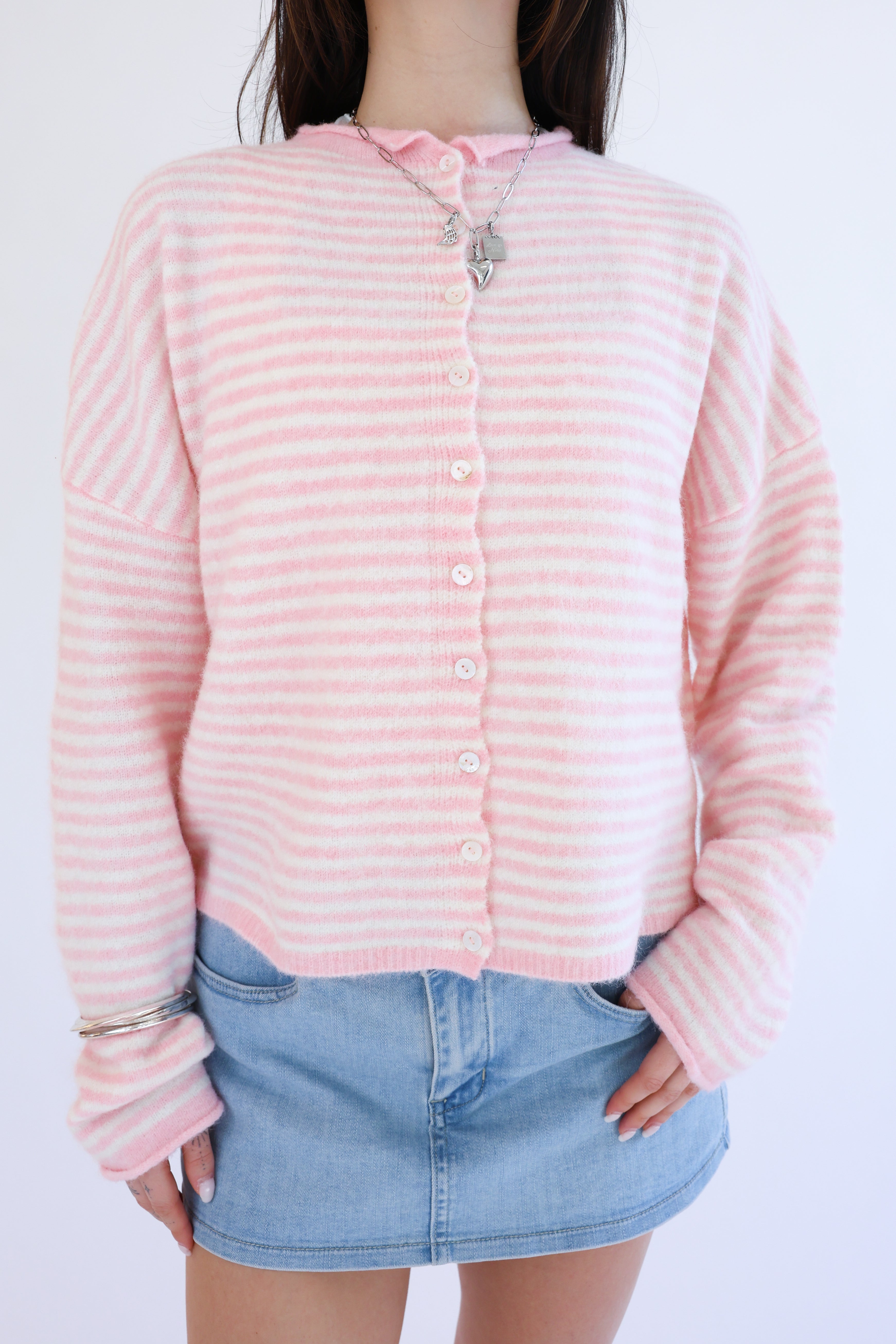 Person wearing a pink striped sweater and denim skirt on a white background