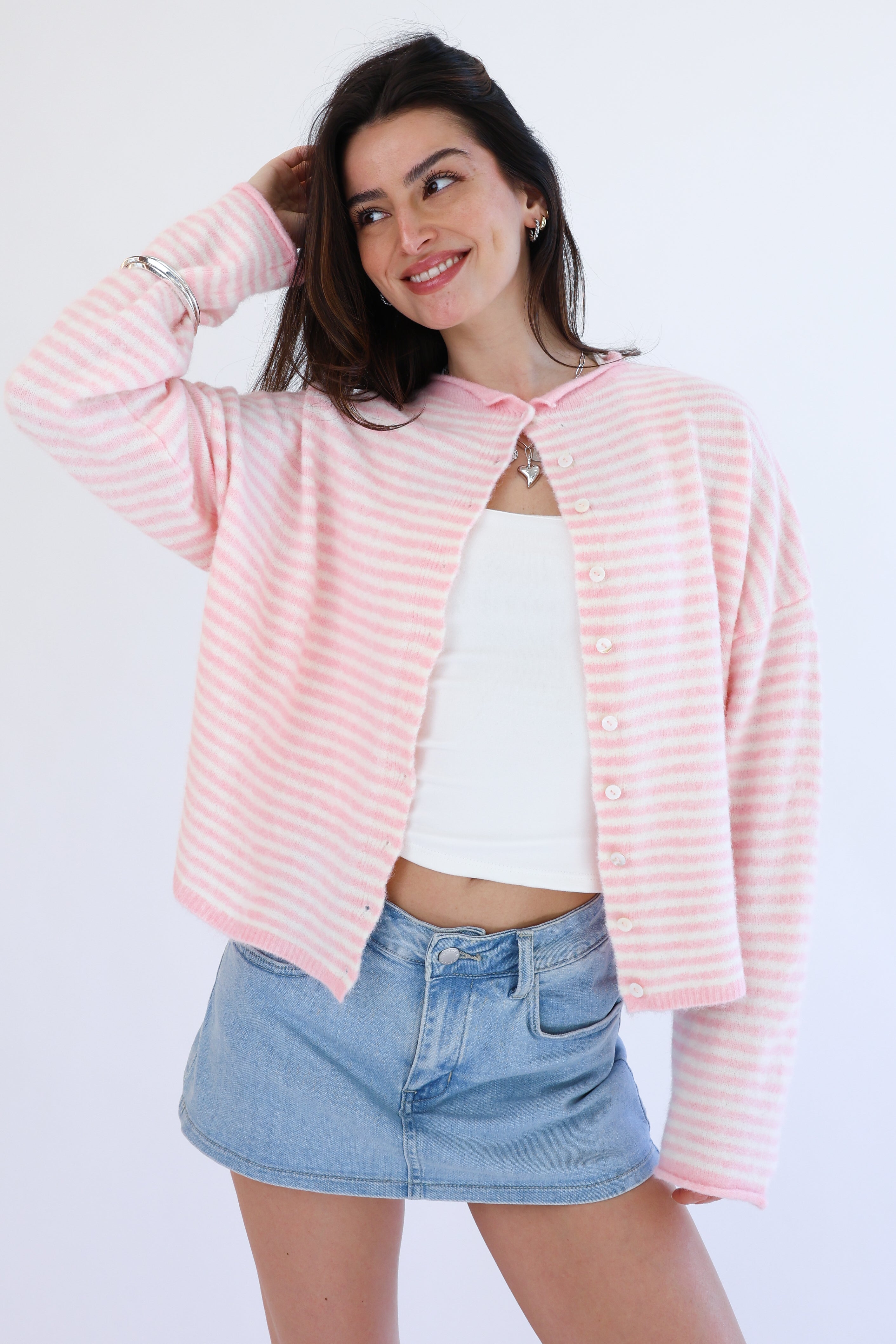 Woman wearing a pink striped cardigan over a white top and denim shorts on a white background