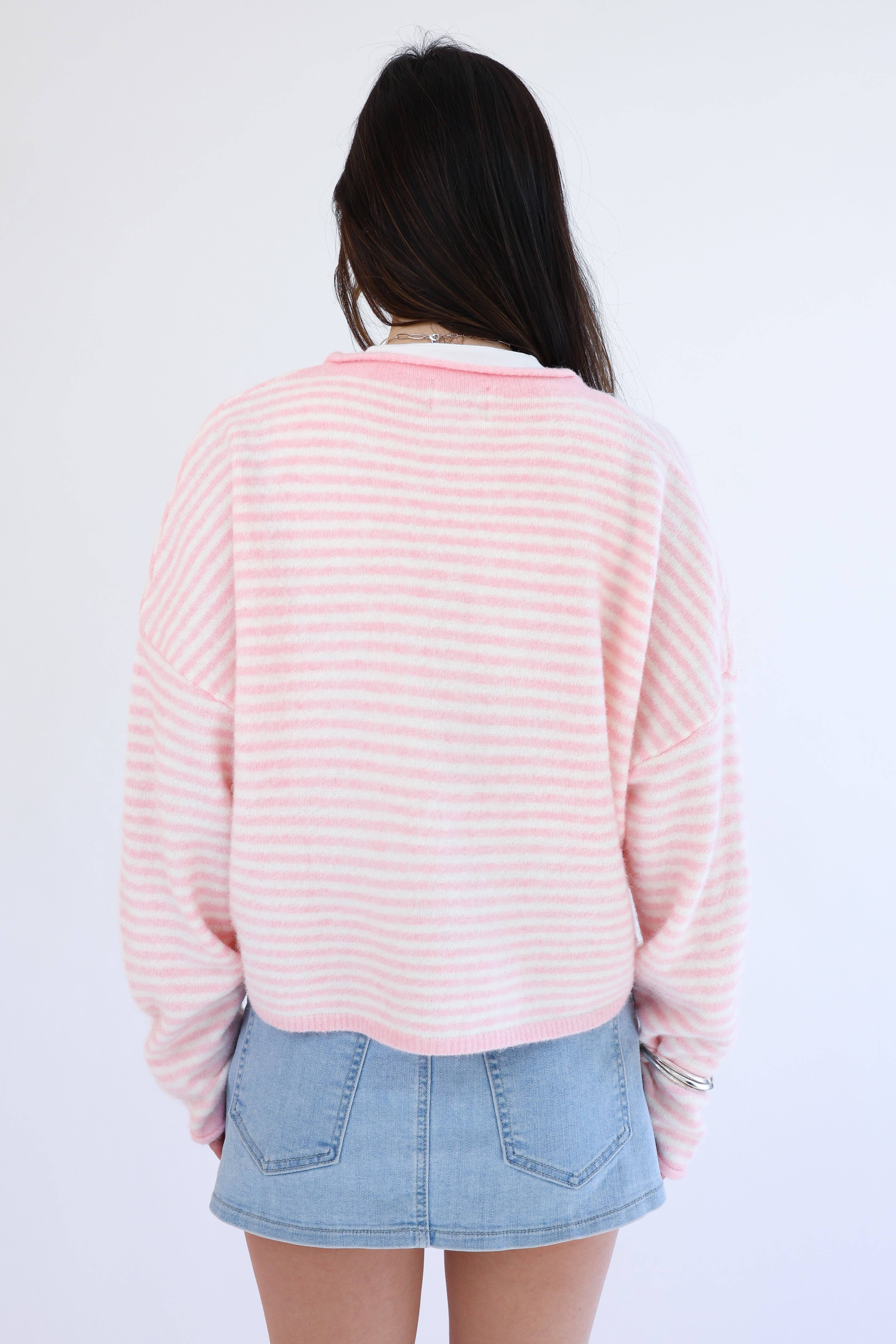 Person wearing a pink striped sweater and denim skirt against a white background