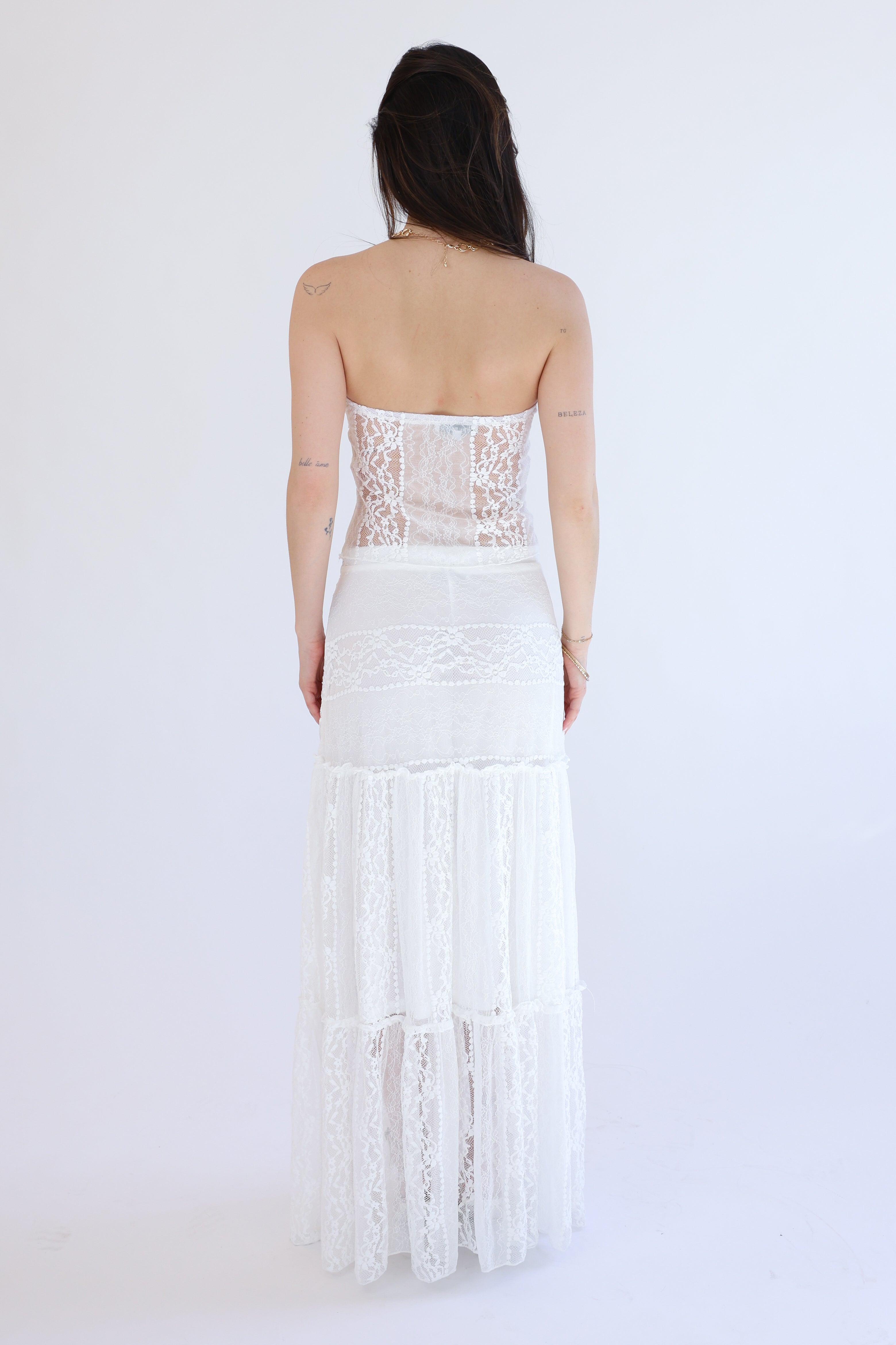 Woman wearing a strapless white lace dress on a plain background