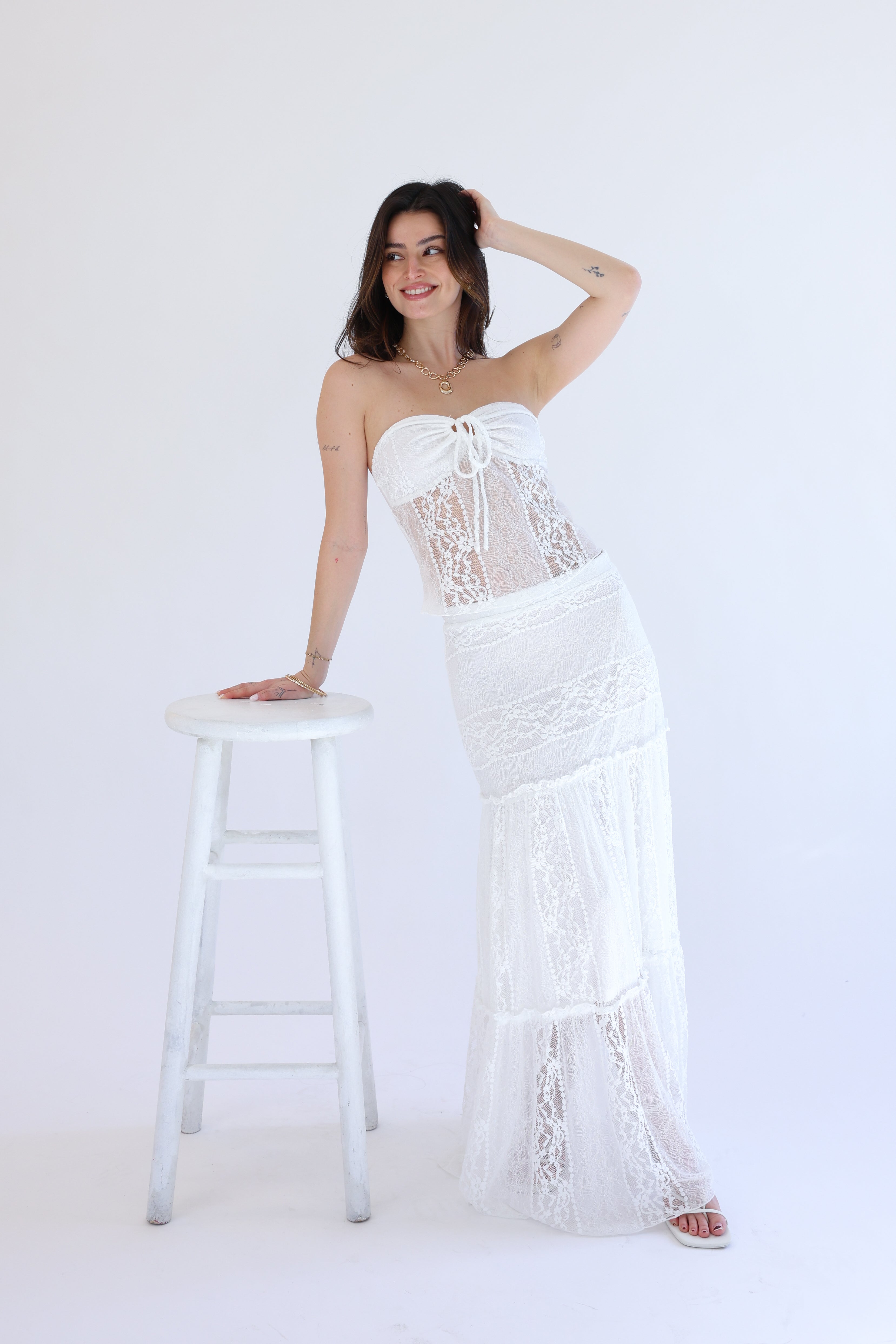 Woman wearing a white lace dress standing next to a white stool on a white background