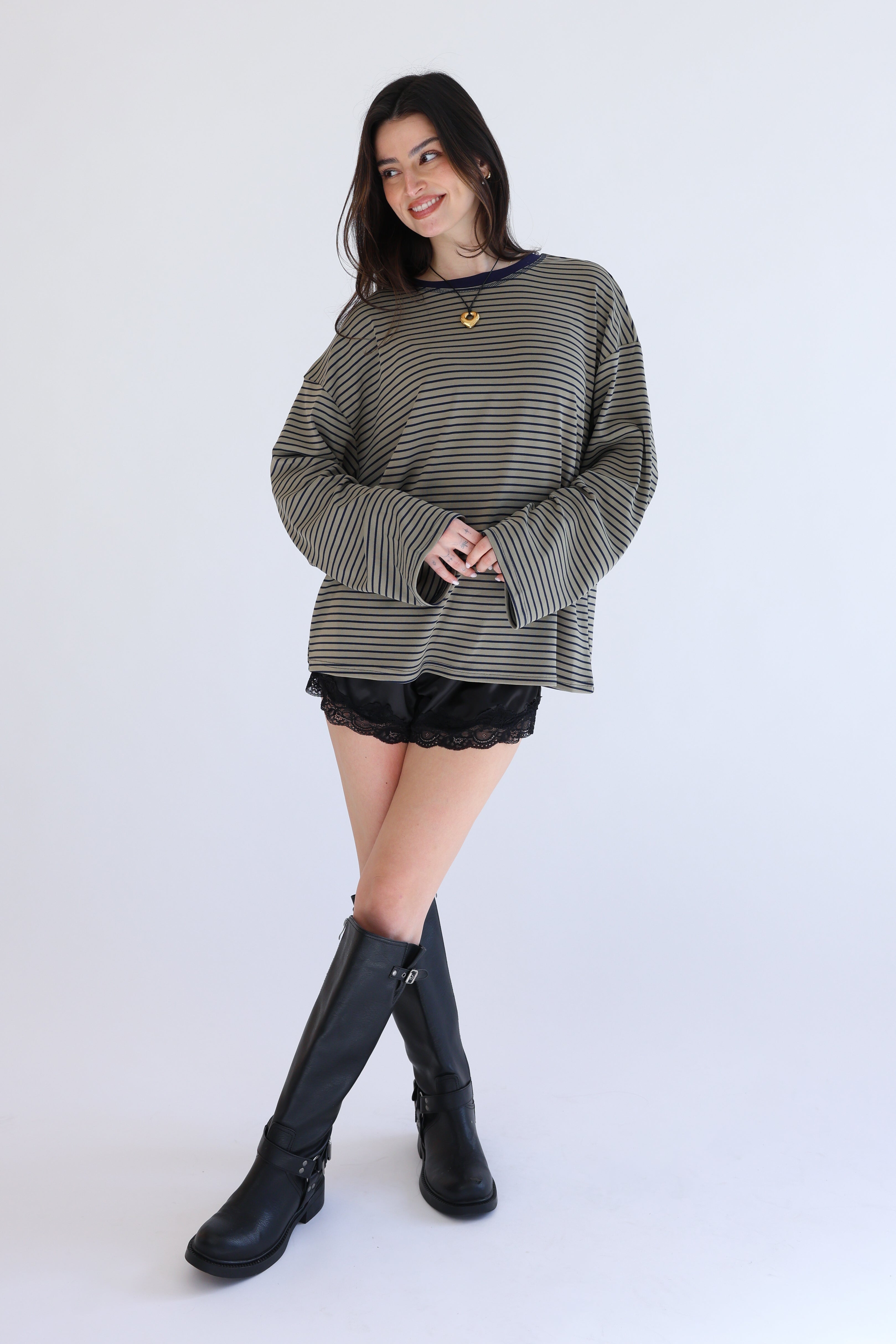 Woman wearing a striped sweater, black shorts, and black knee-high boots on a white background