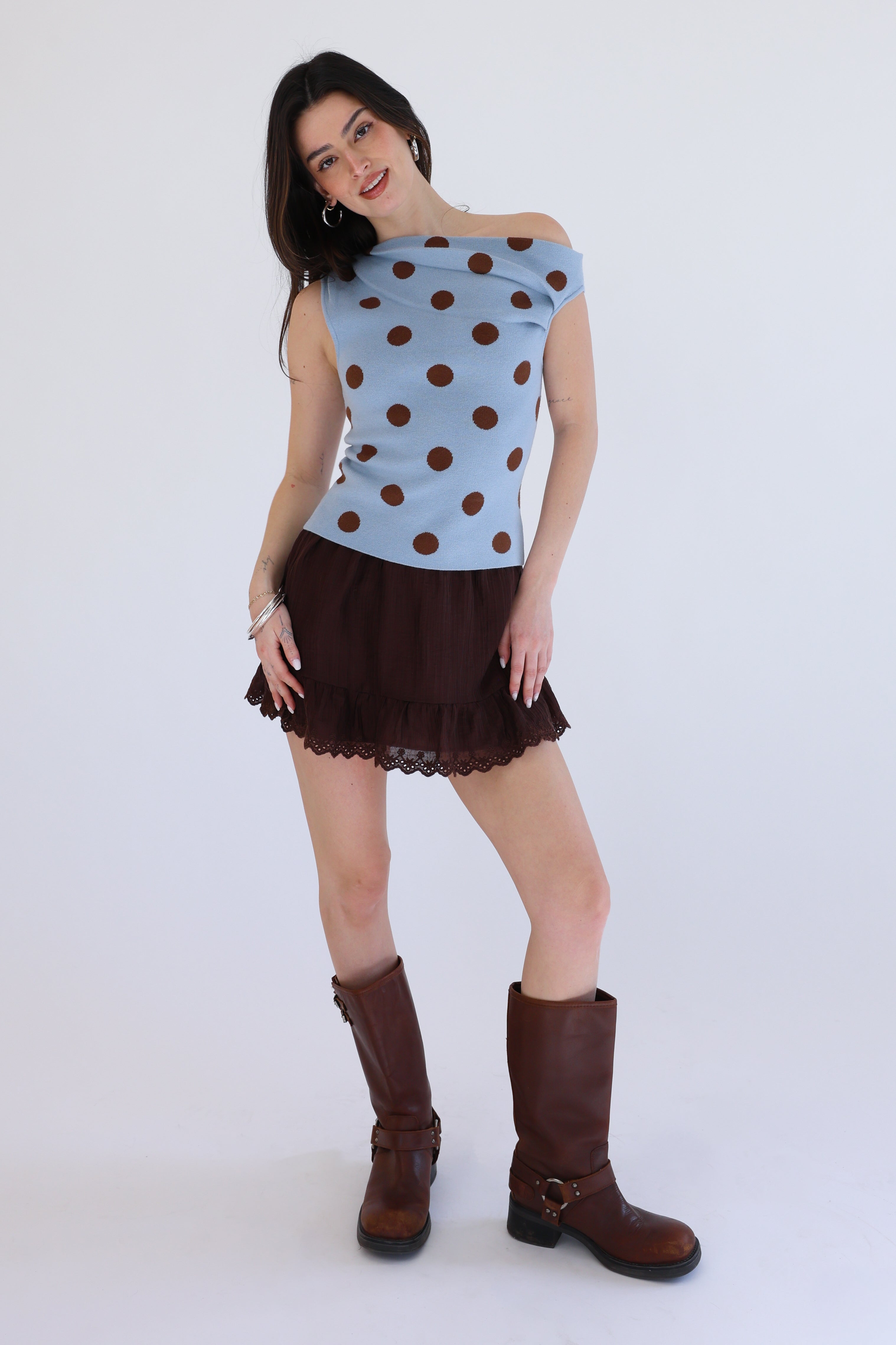 Woman wearing a blue top with brown polka dots and a brown skirt on a white background
