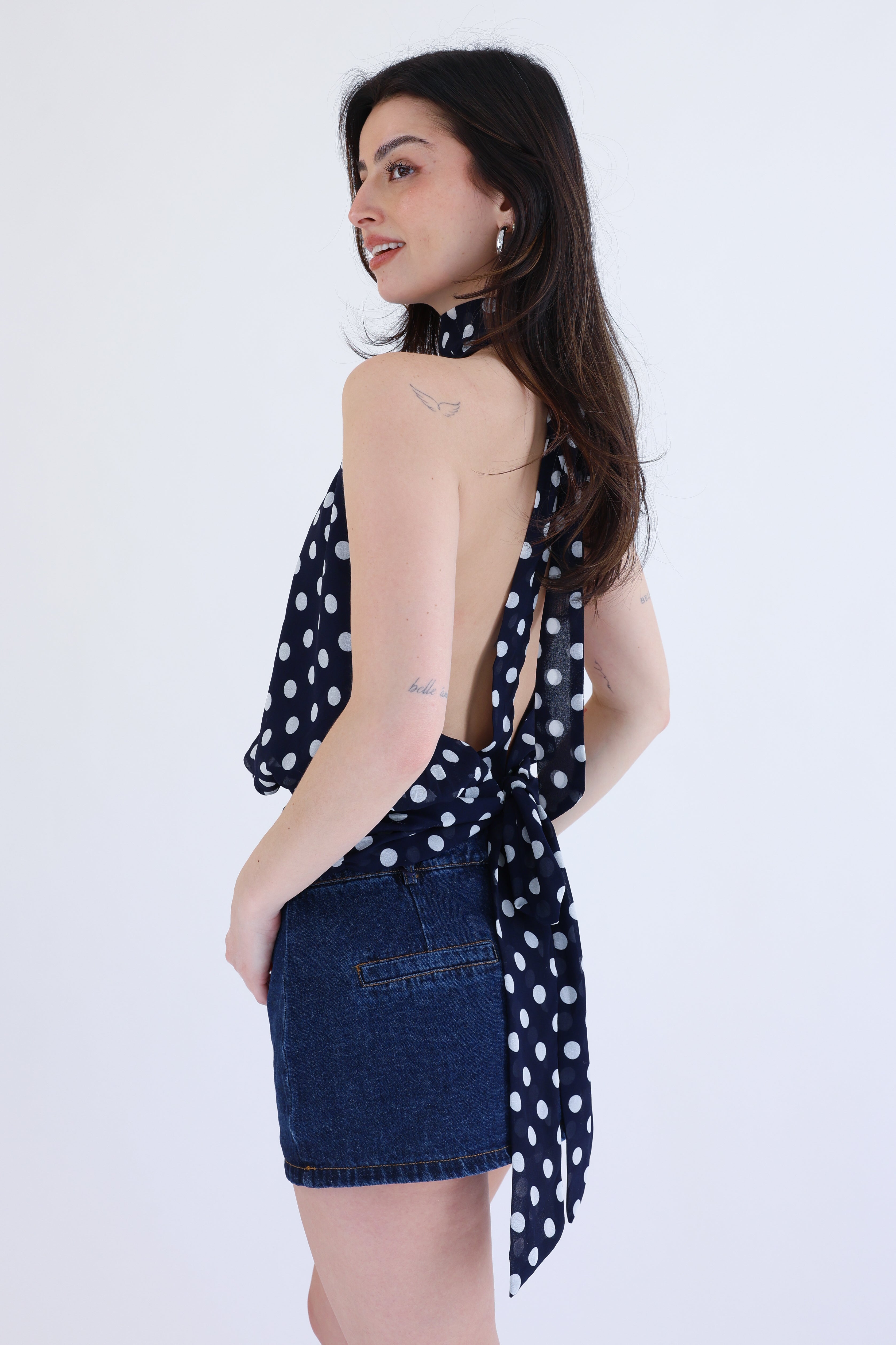Woman wearing a polka dot top and denim skirt on a white background