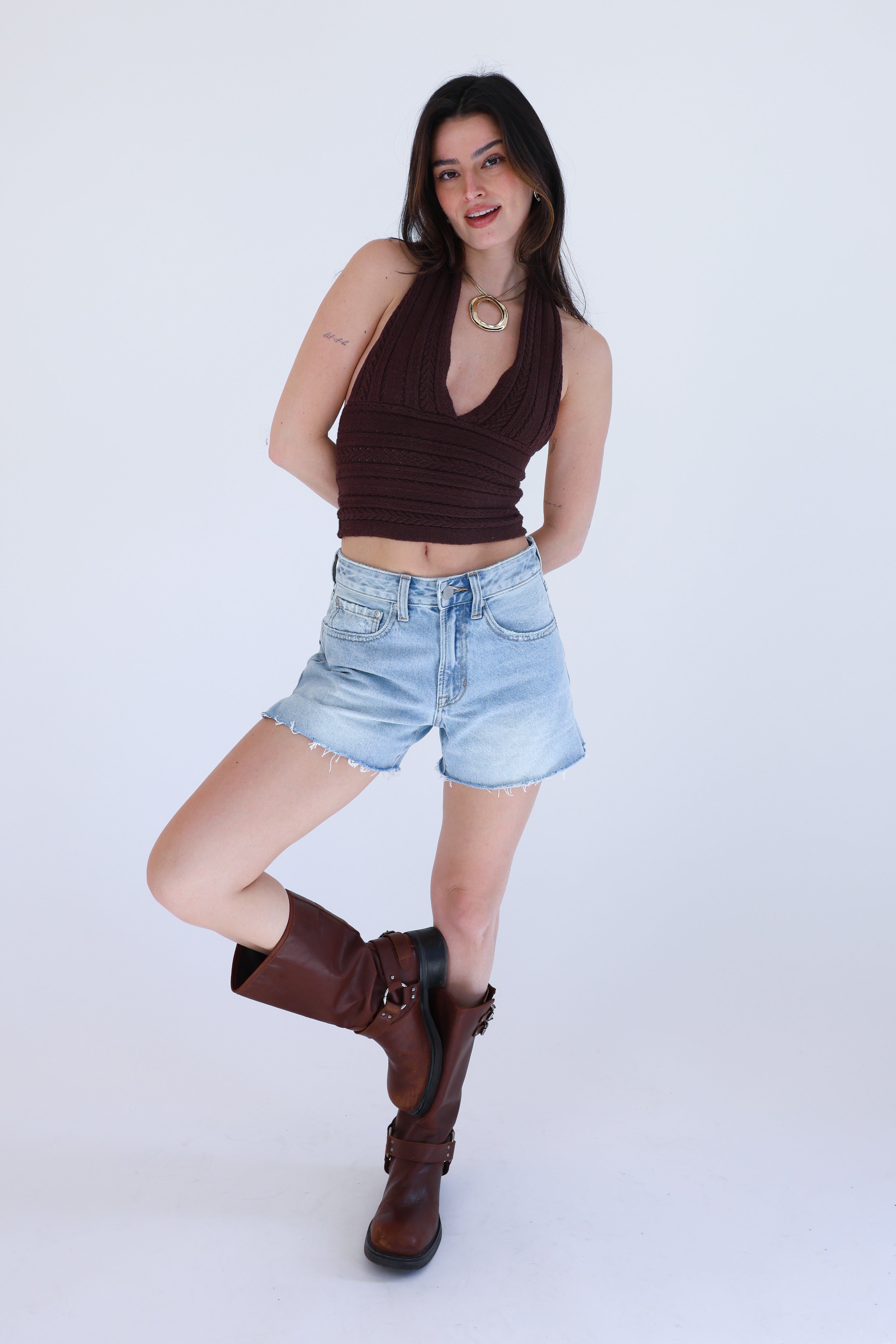 Woman wearing a brown top, denim shorts, and brown boots on a white background