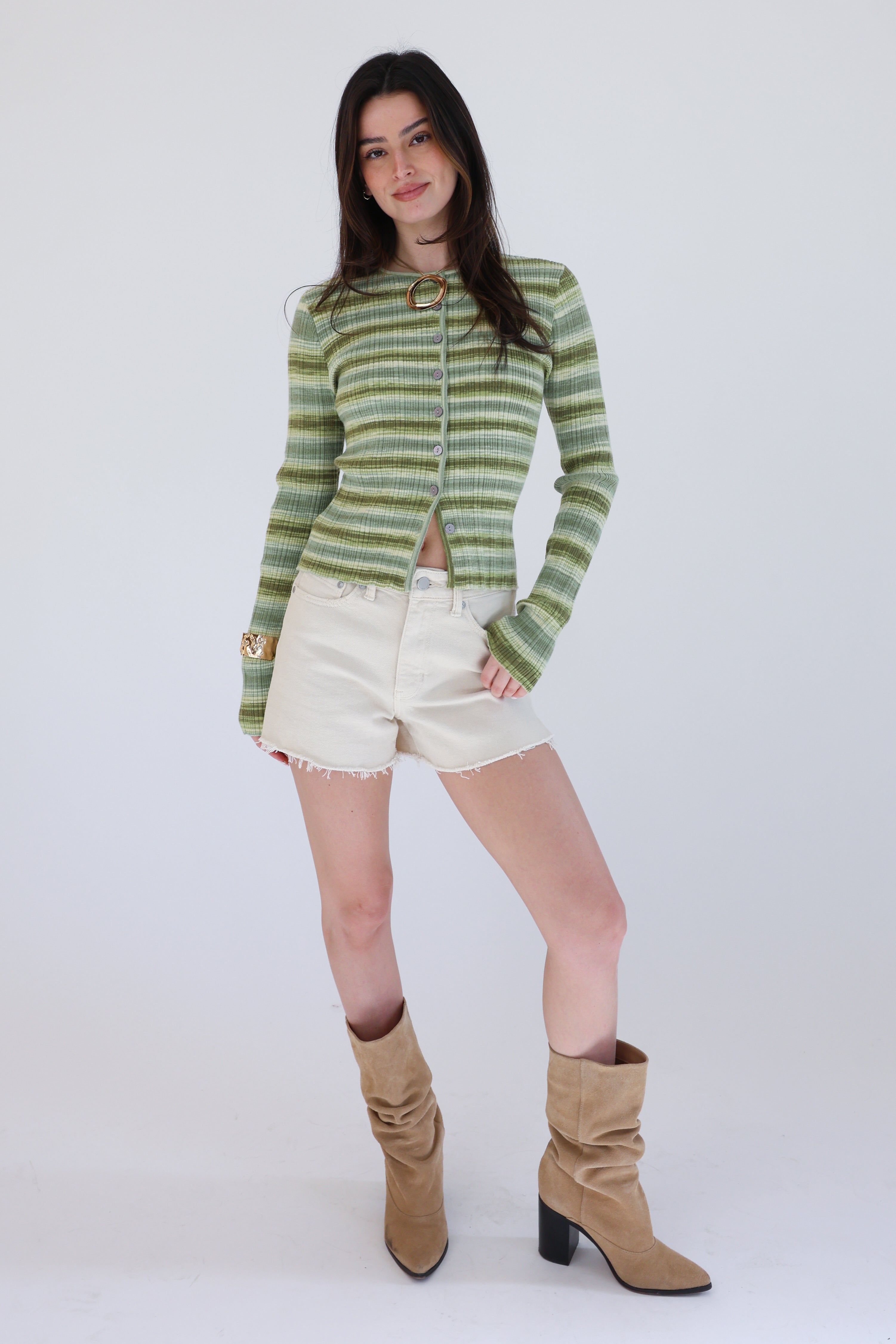 Woman wearing a green striped sweater, white shorts, and tan boots on a white background