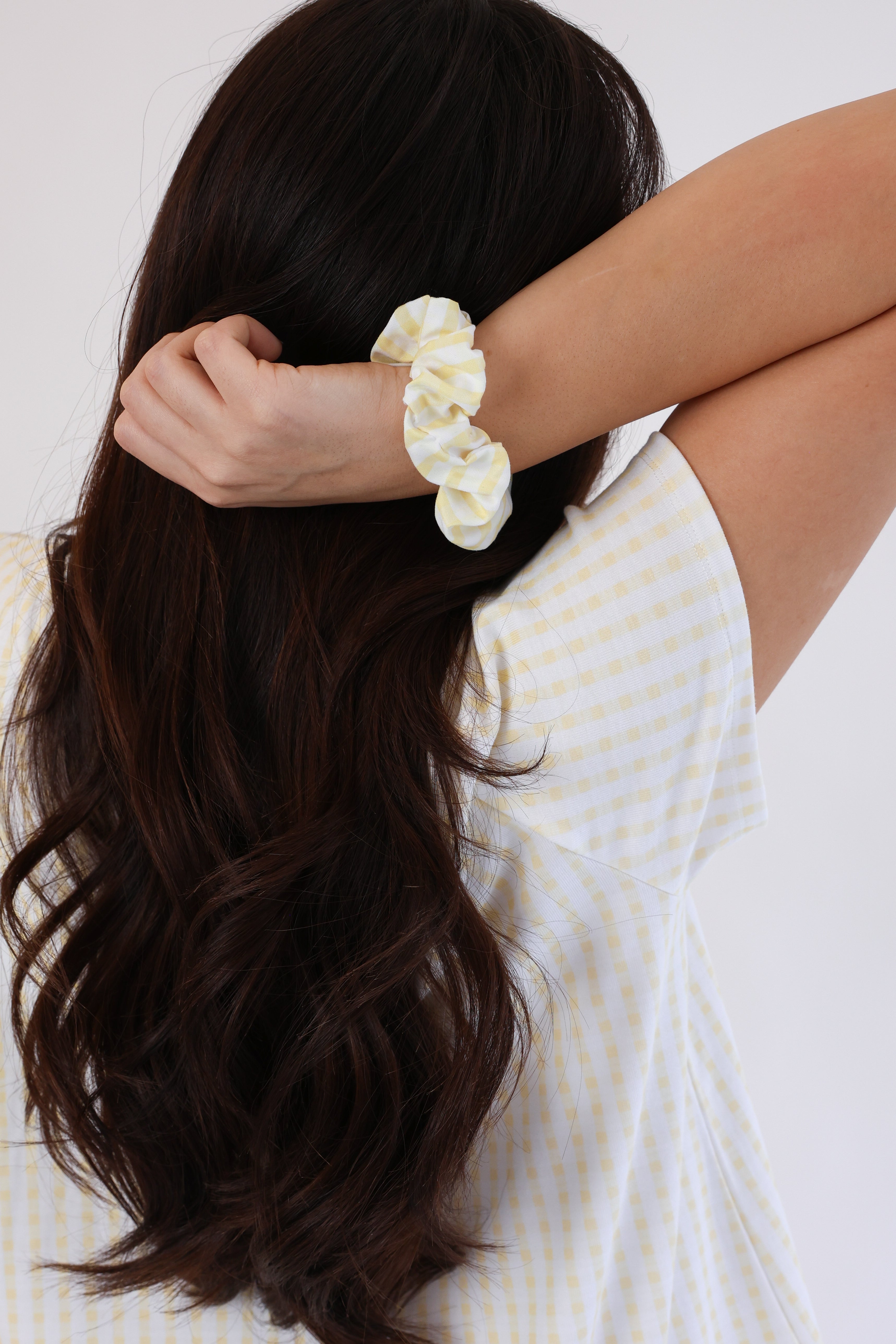 Woman with long dark hair wearing a white scrunchie, sitting on a white couch.