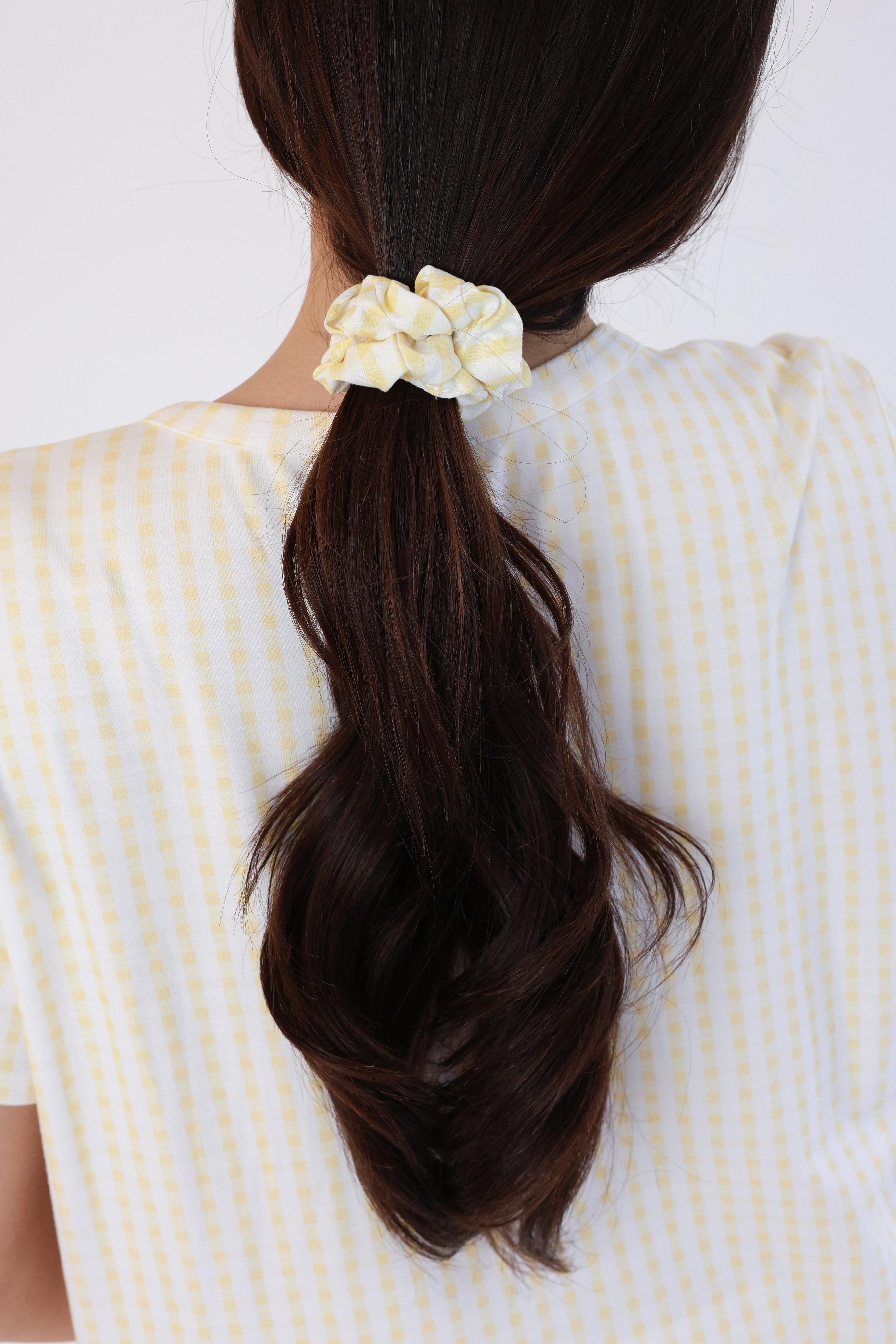 Person with a ponytail held by a yellow scrunchie against a white background