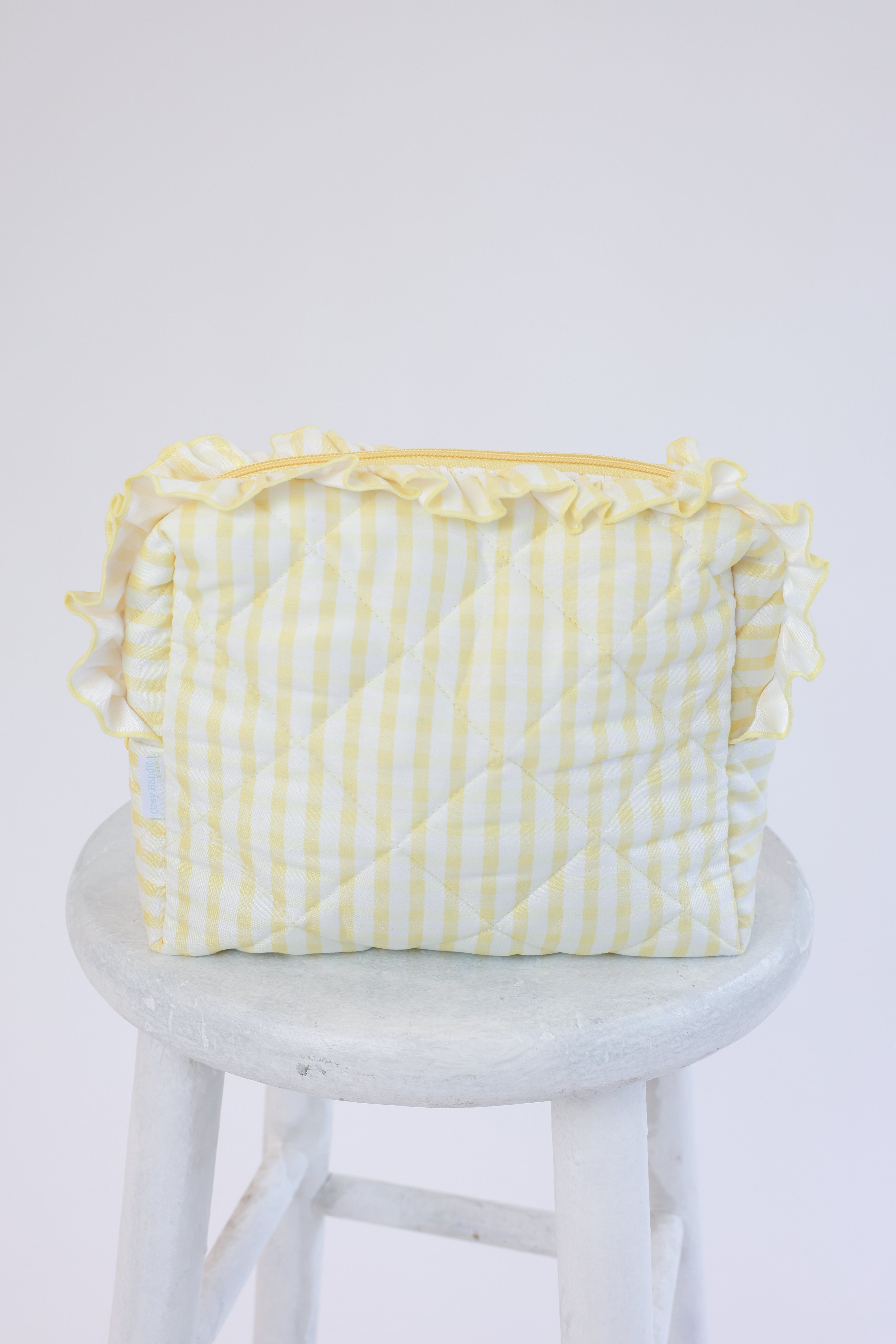 Yellow checkered bag with ruffles on a white stool against a white background
