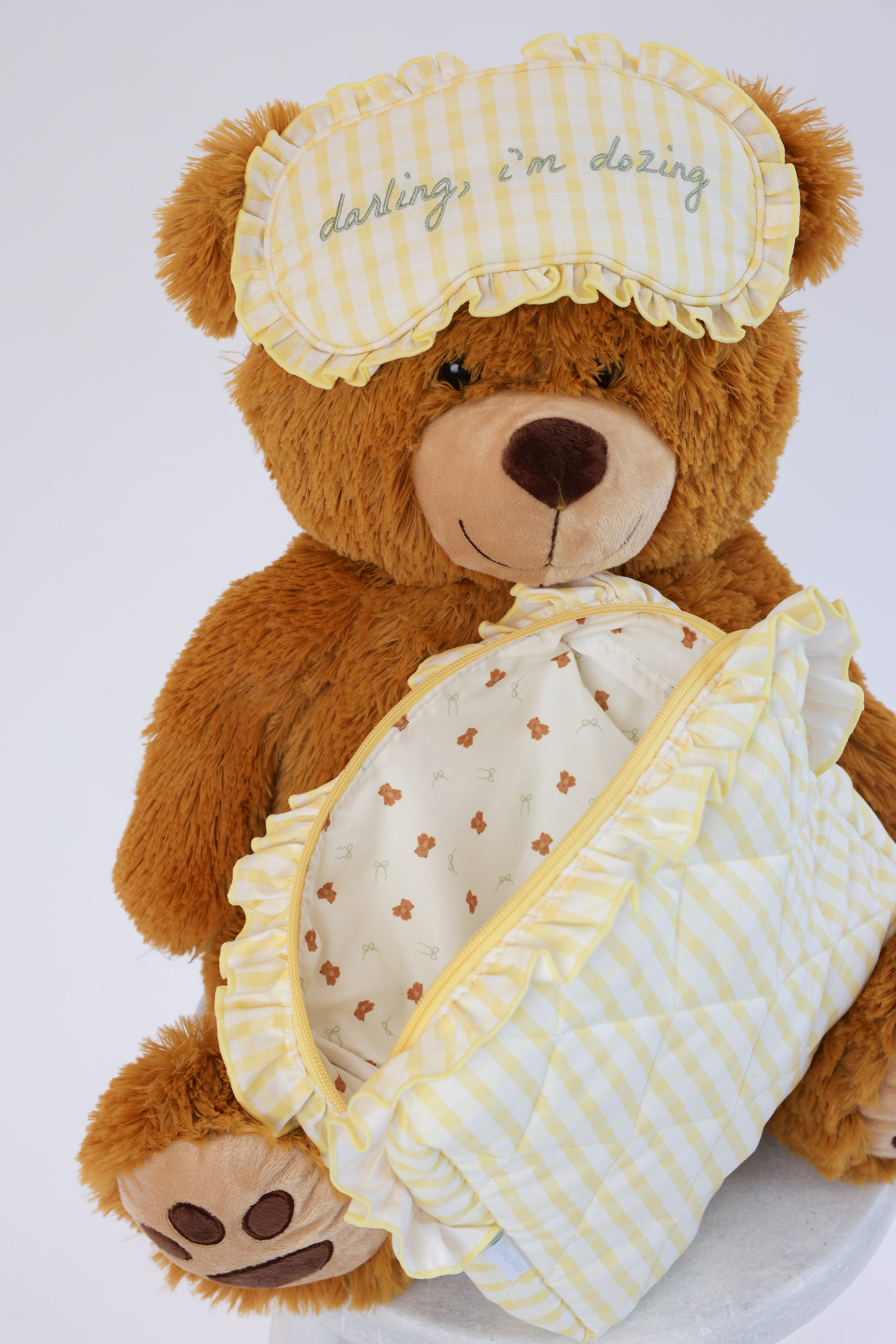 Teddy bear wearing a sleep mask and holding a blanket on a white background