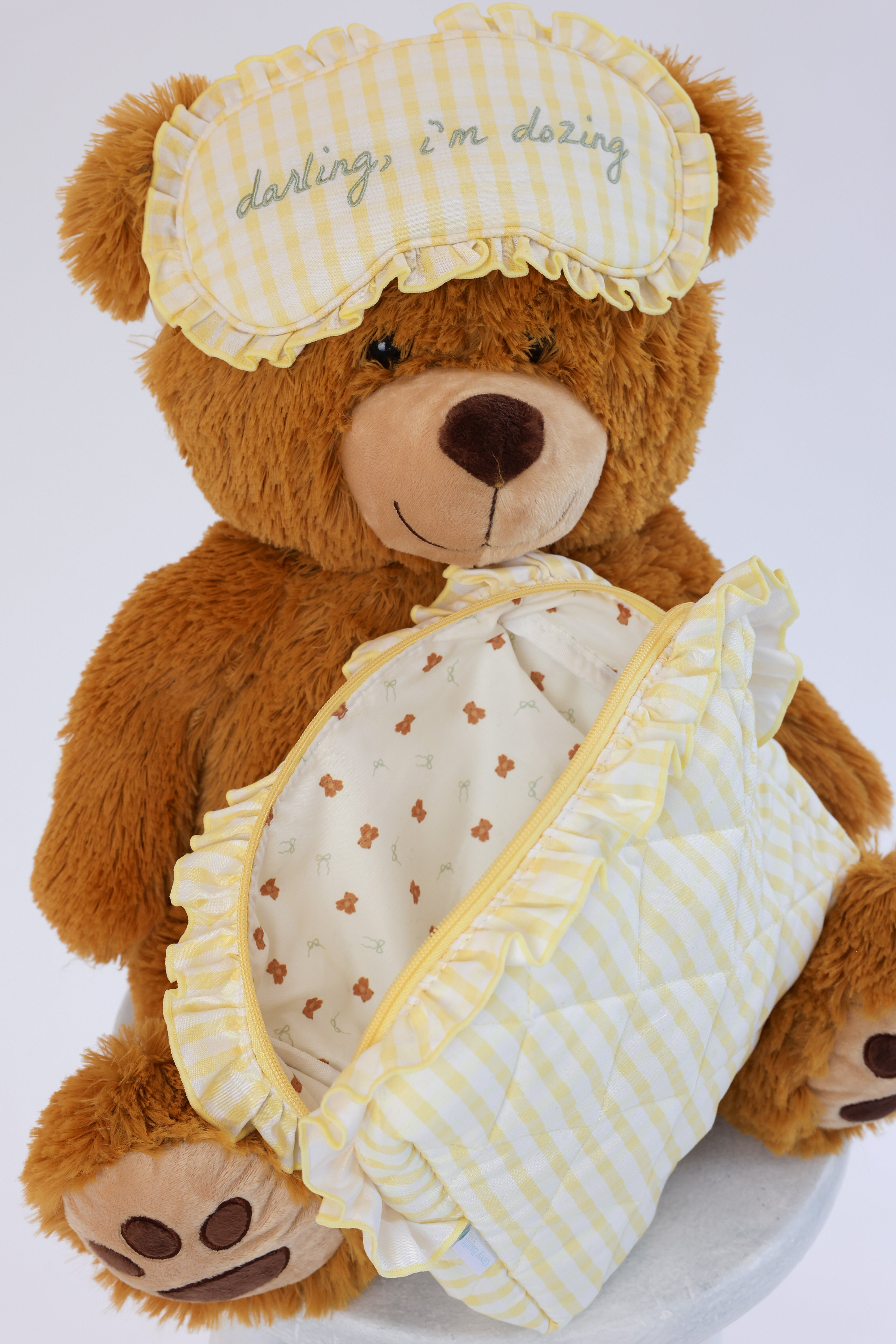Teddy bear wearing a sleep mask and holding a blanket with paw prints on a white background