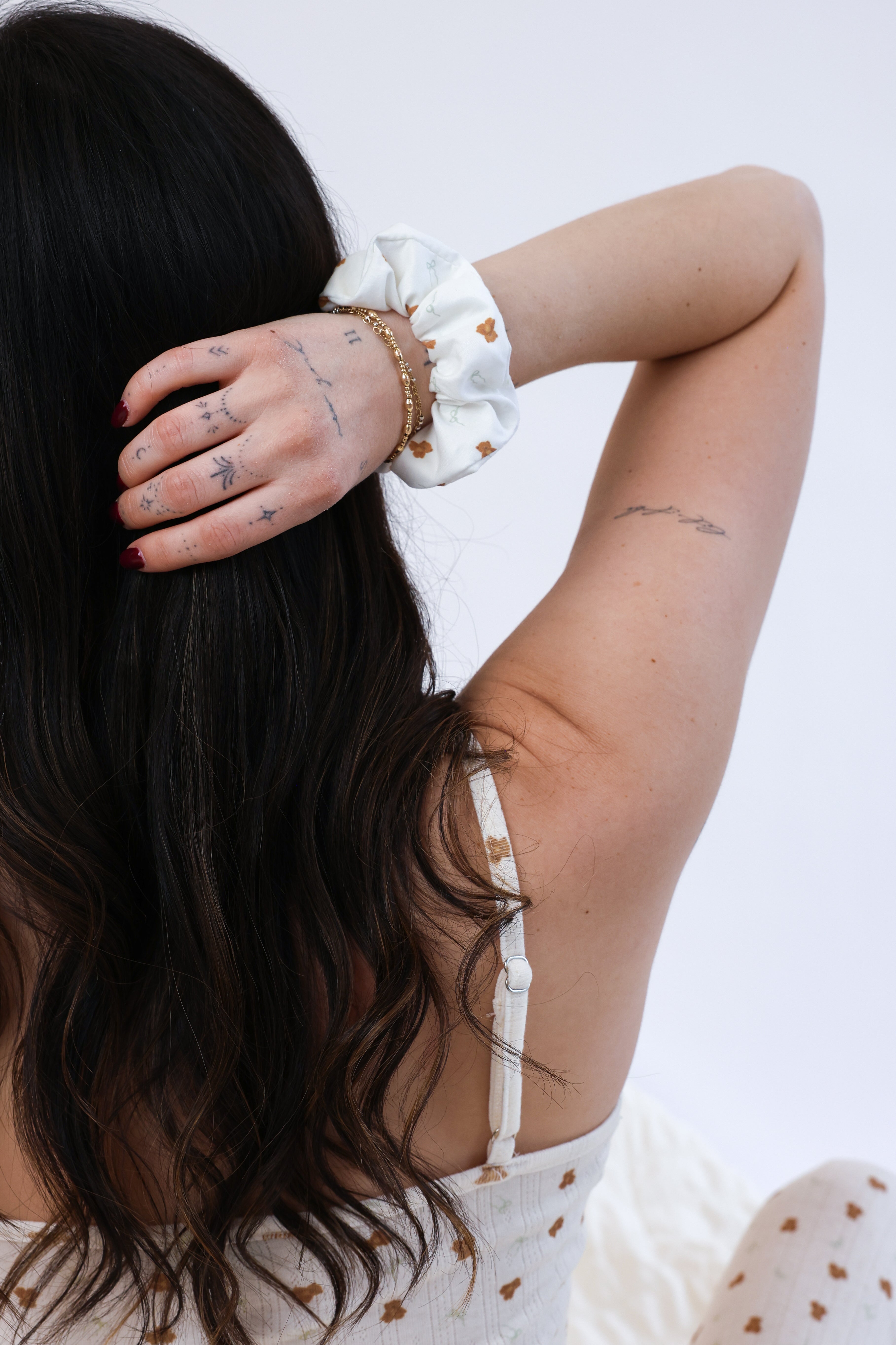 Woman with tattoos on her arm and neck, wearing a white top with brown patterns, against a plain background.