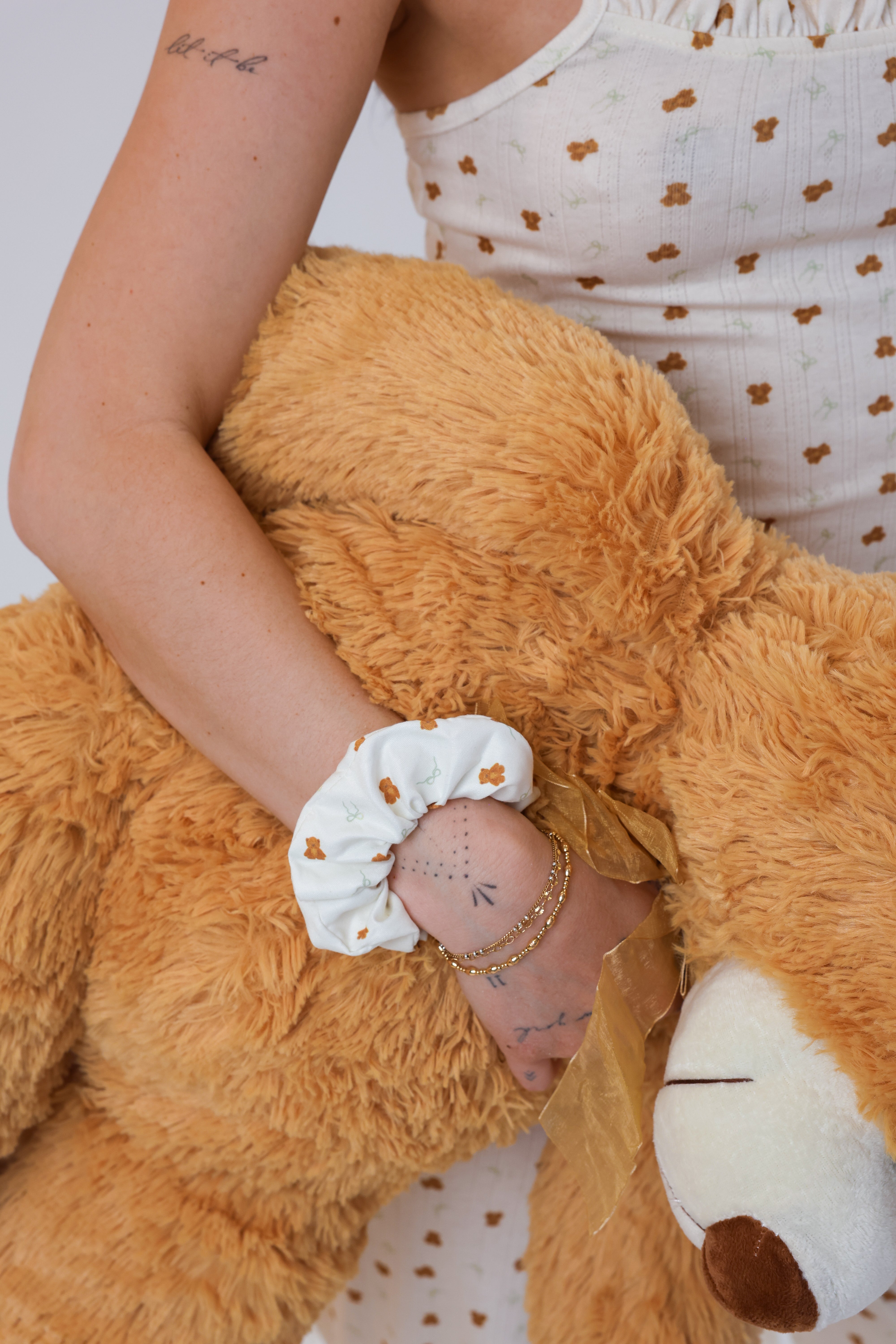 Person holding a large brown teddy bear wearing a white sleeve with brown polka dots.