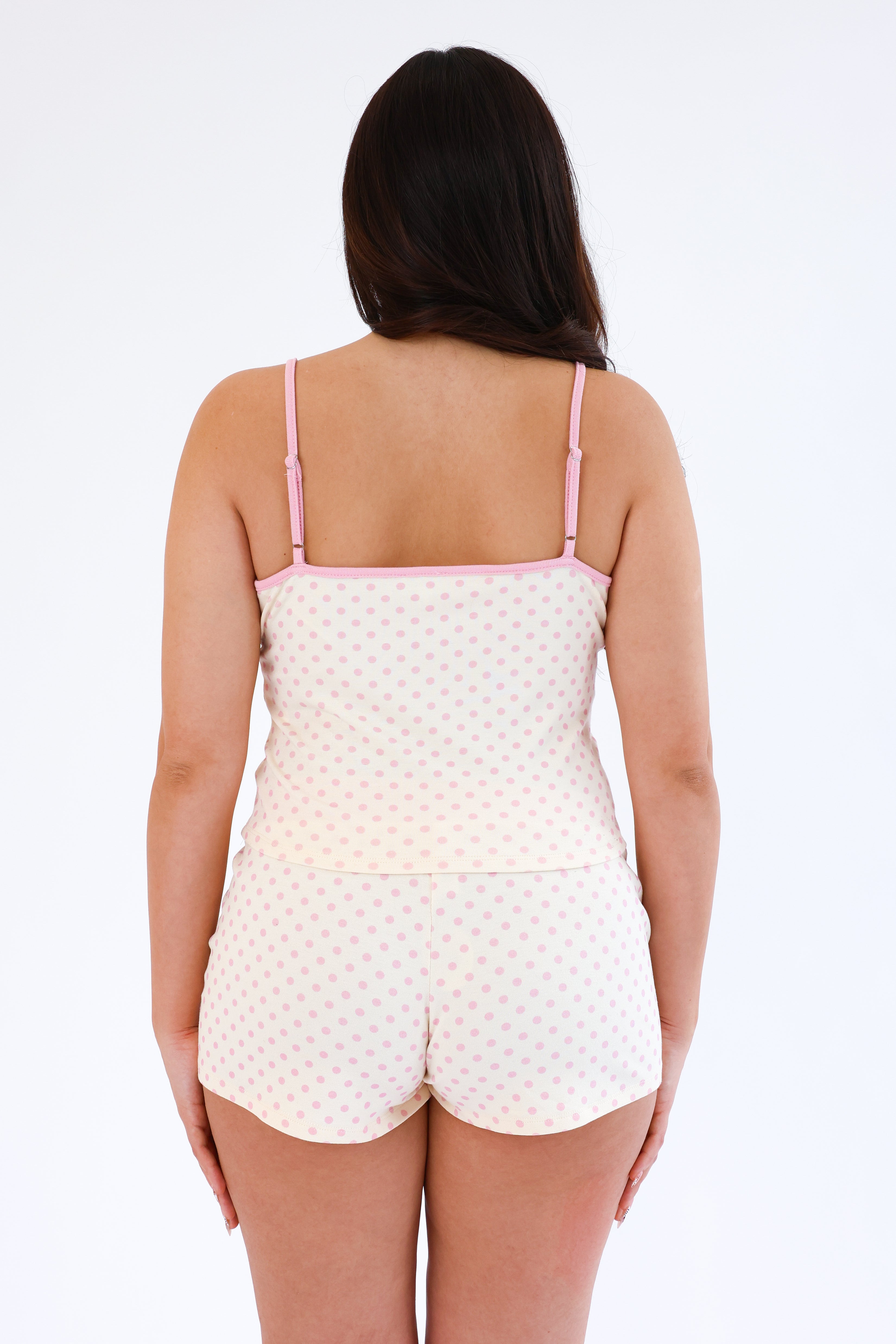 Woman wearing a white polka dot pajama set with pink straps on a white background