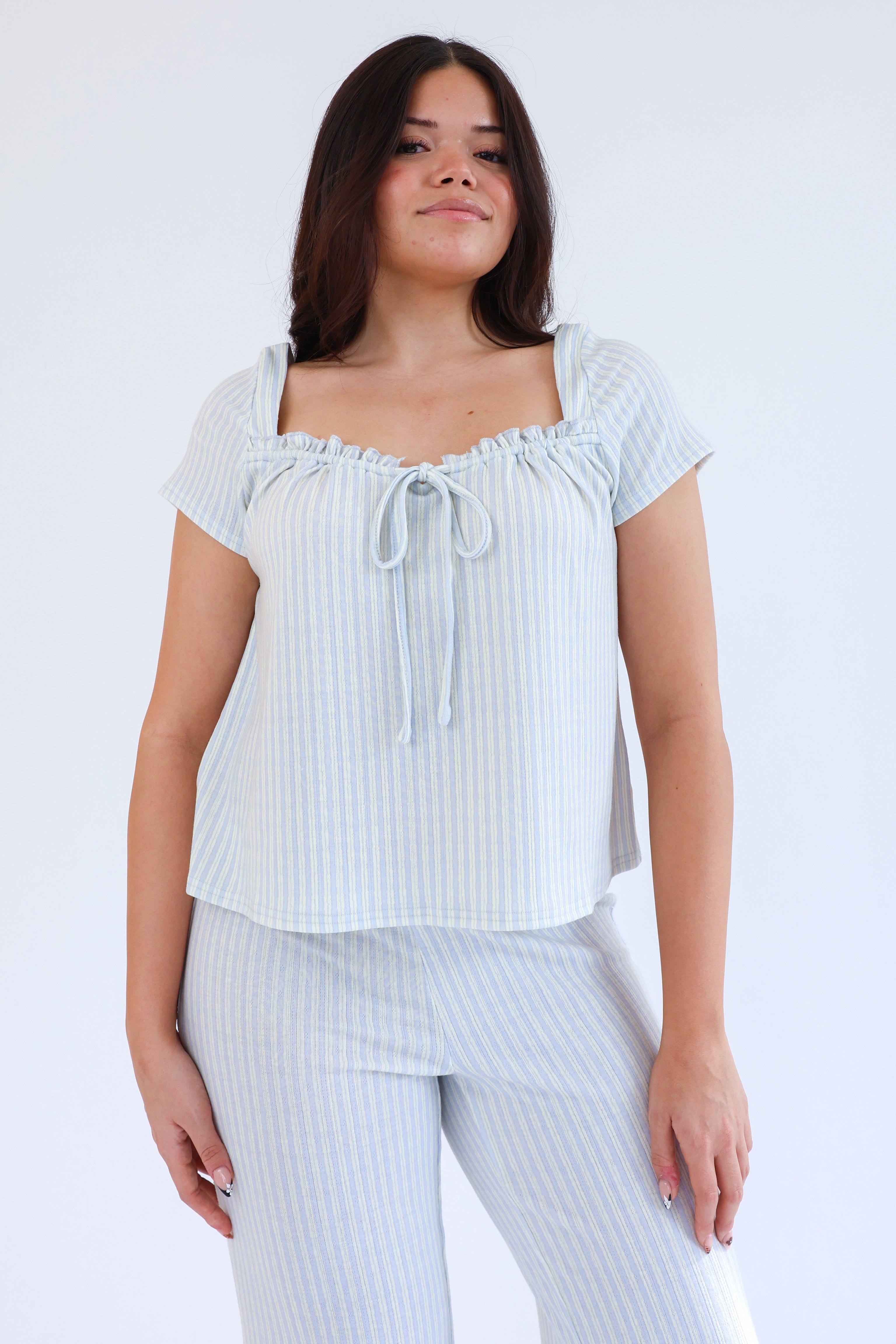 Woman wearing a light blue striped top and pants on a white background
