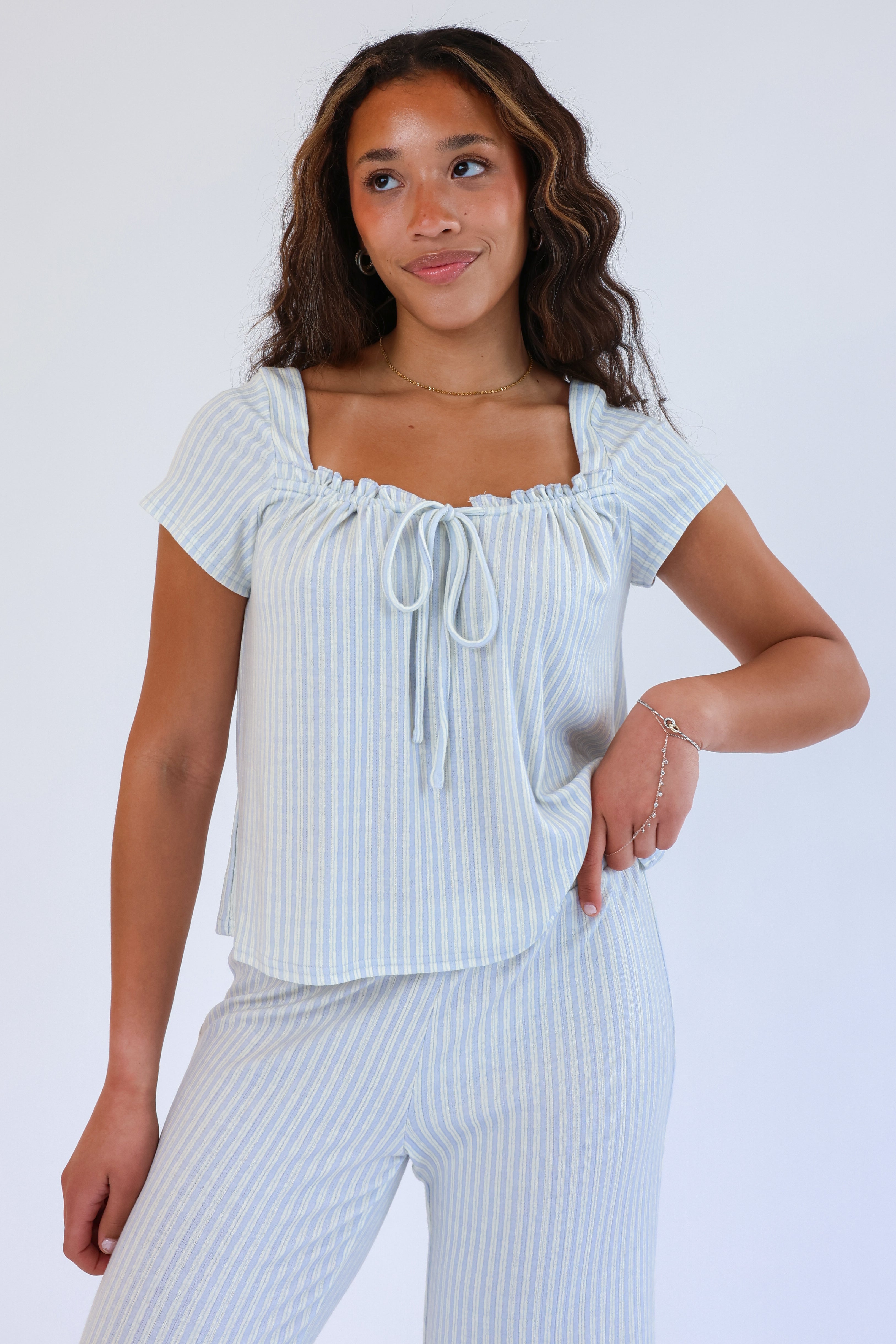 Woman wearing a light blue ribbed top and pants against a white background