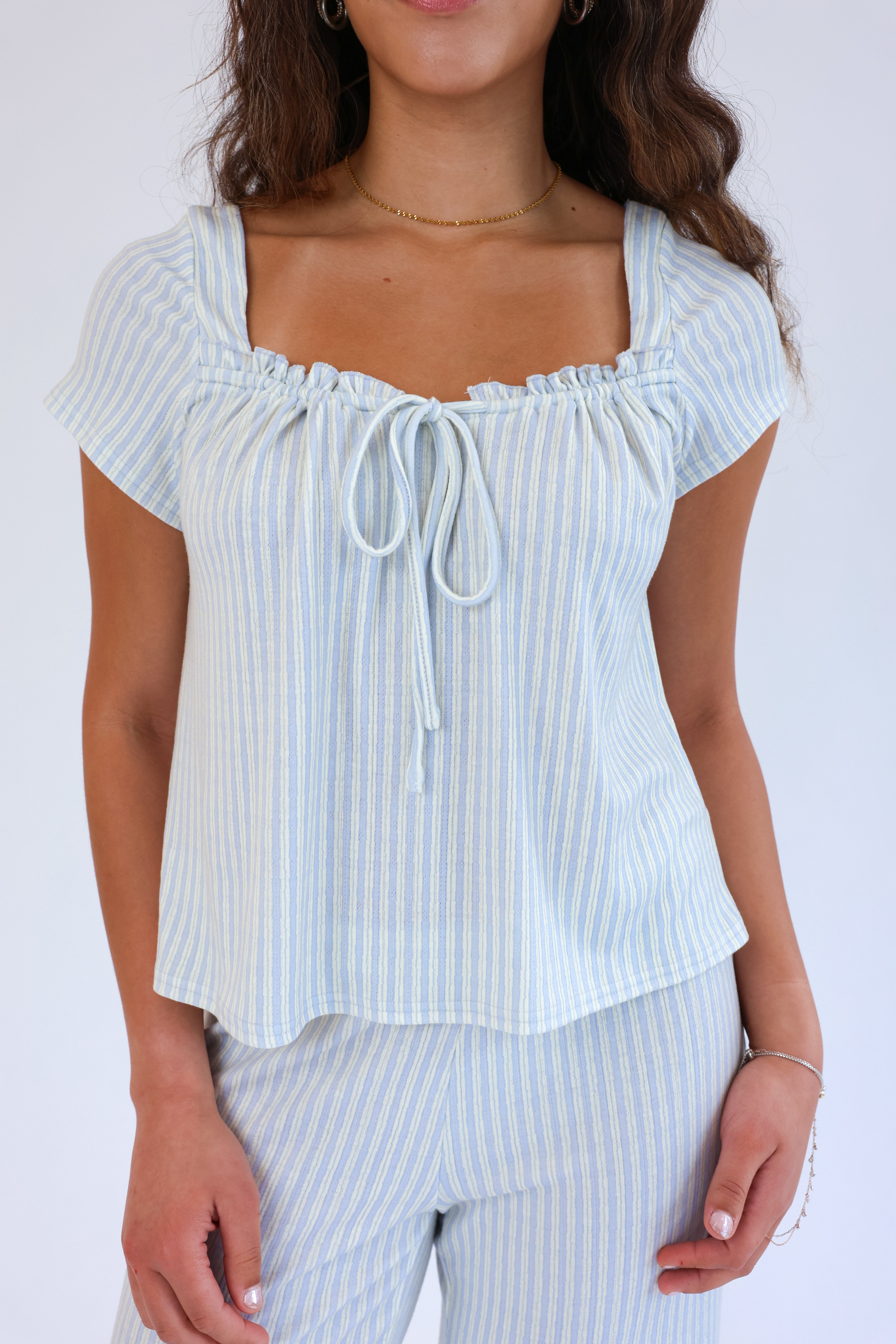 Woman wearing a light blue striped top and pants against a white background