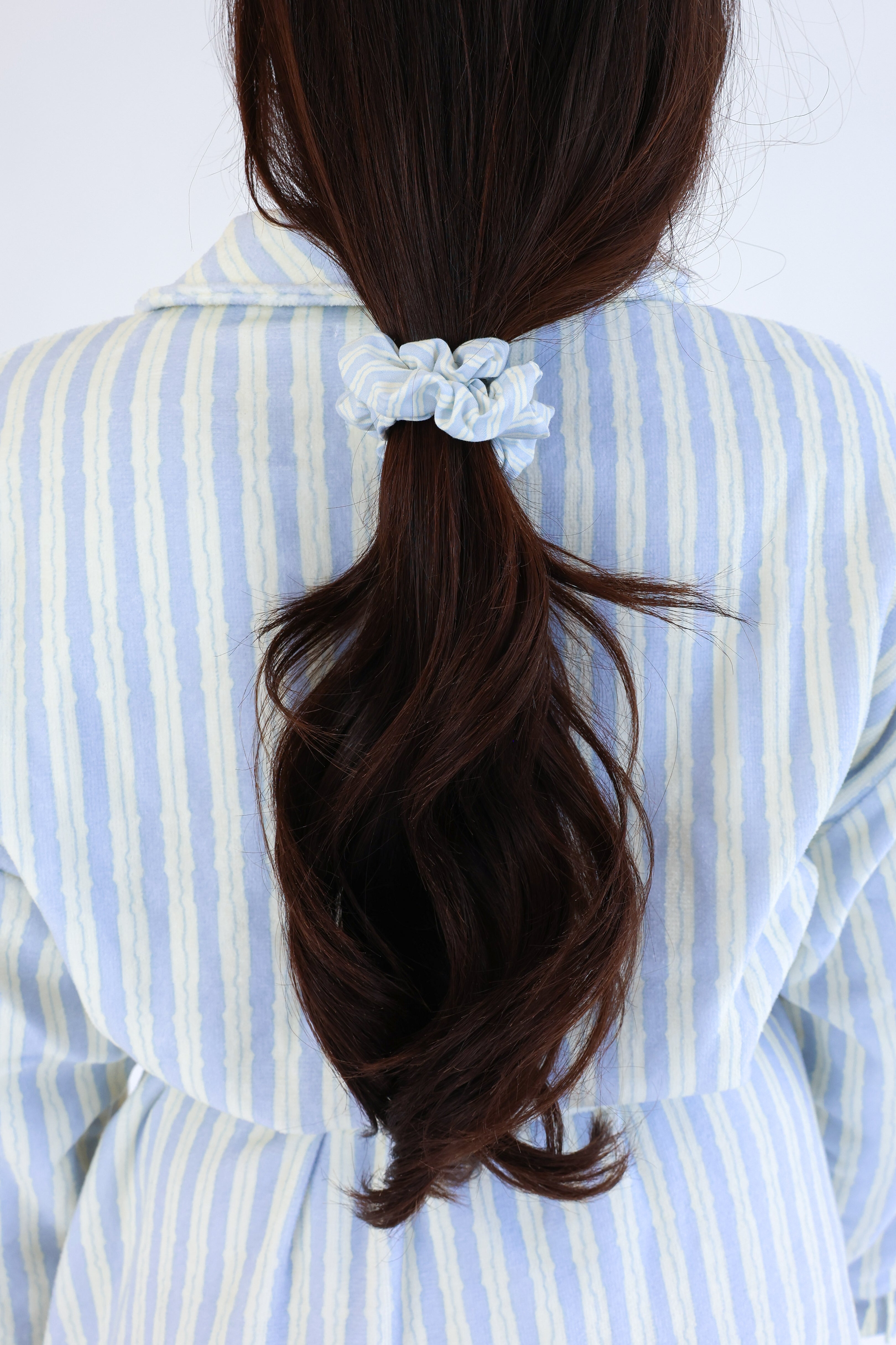 Person with long brown hair tied in a ponytail with a white scrunchie, wearing a blue and white striped shirt.