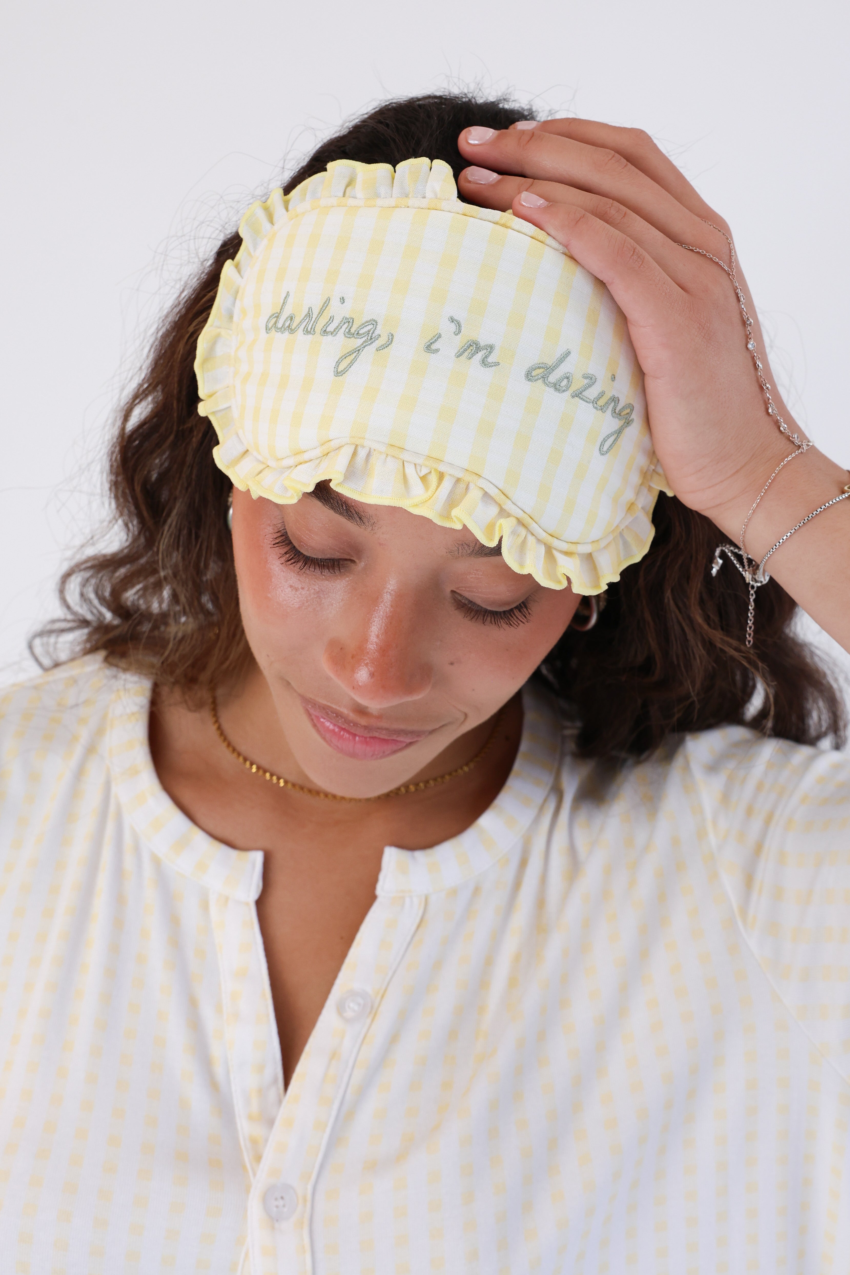 Woman wearing a yellow checkered sleep mask with text on a white background