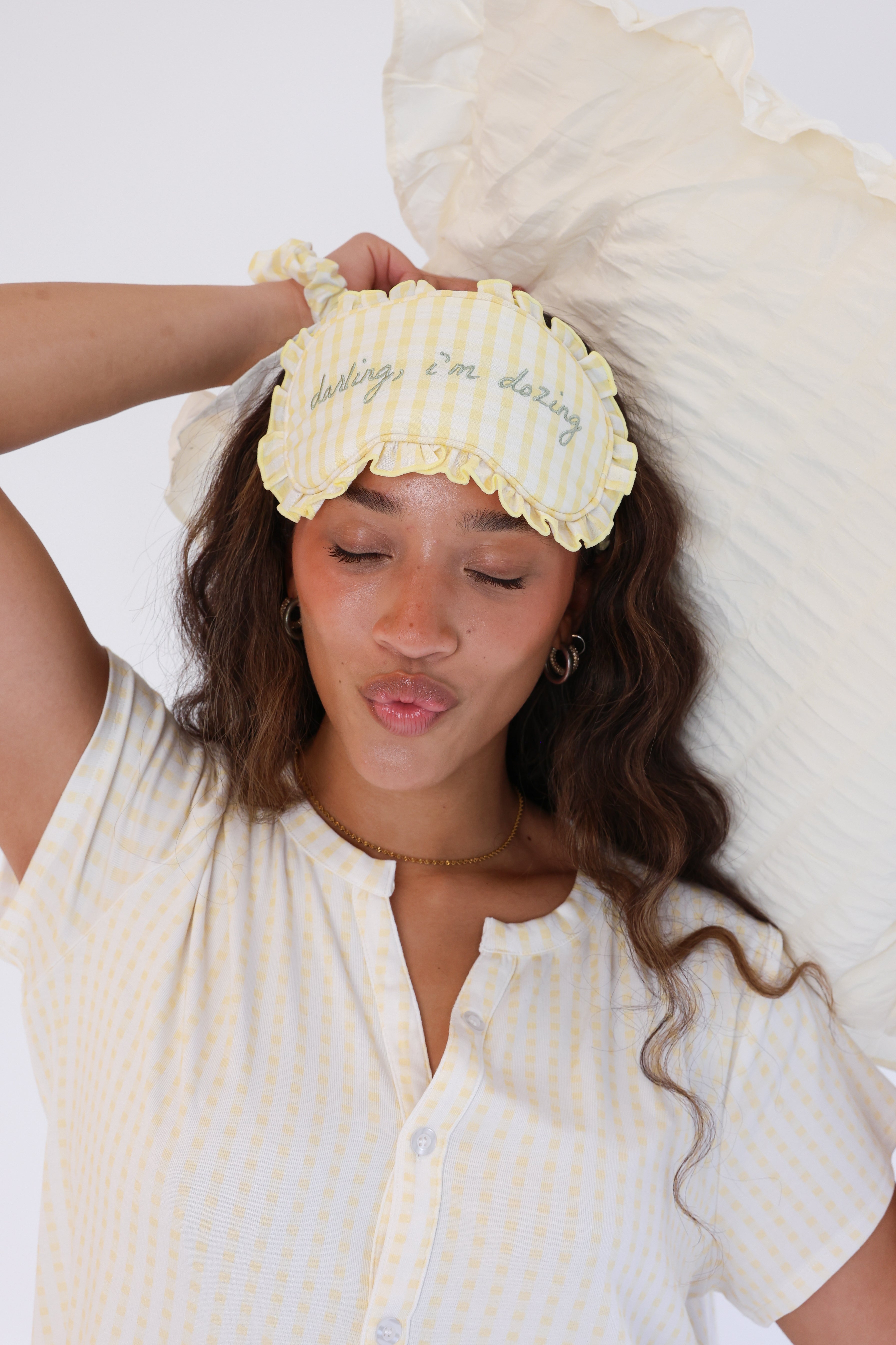 Woman wearing a yellow sleep mask with text, sitting against a white pillow.