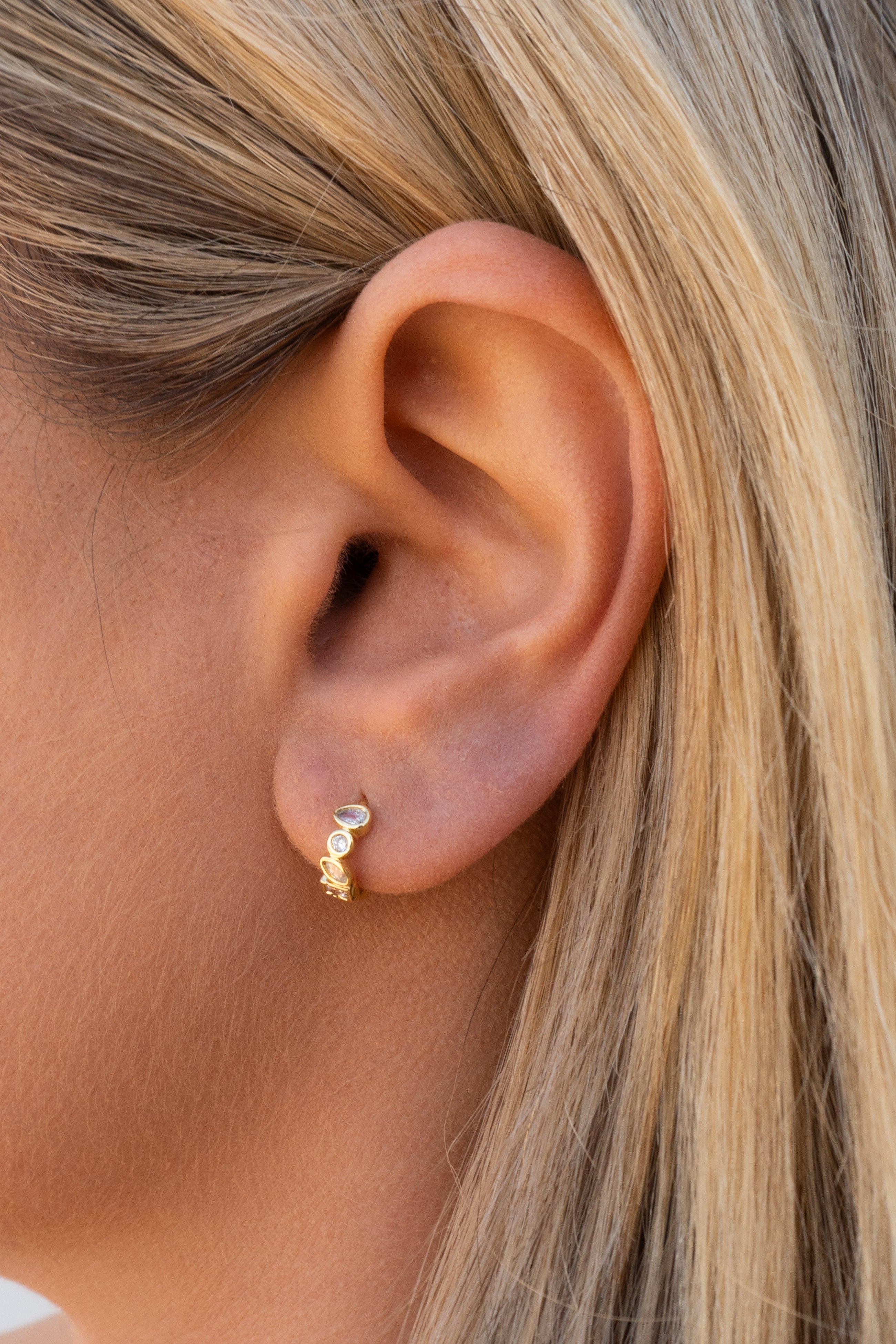 Close-up of an ear wearing a gold earring with a clear gemstone.