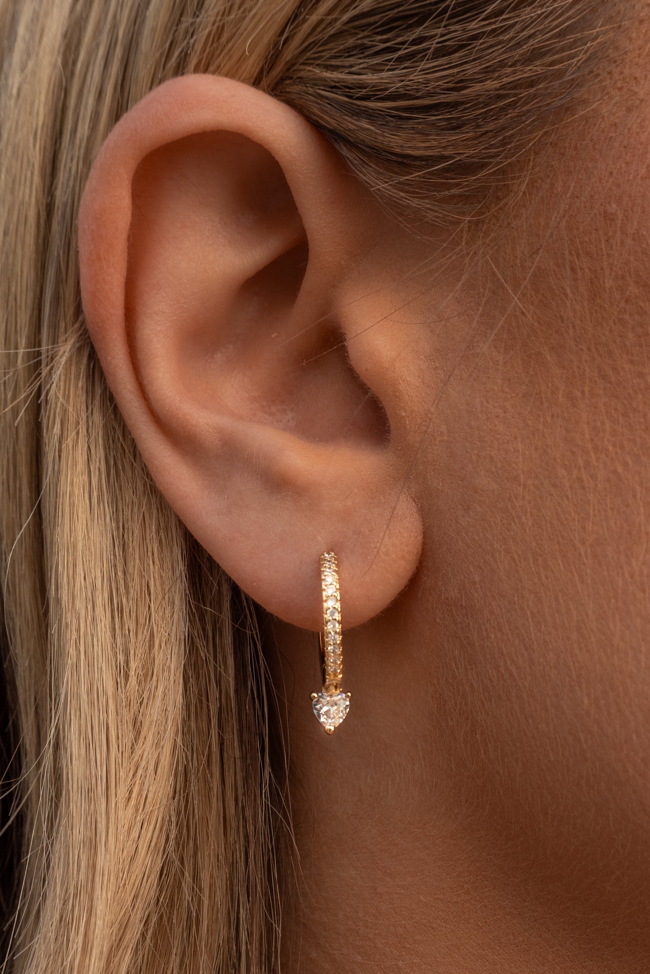 Close-up of an ear wearing a rose gold hoop earring on a neutral background