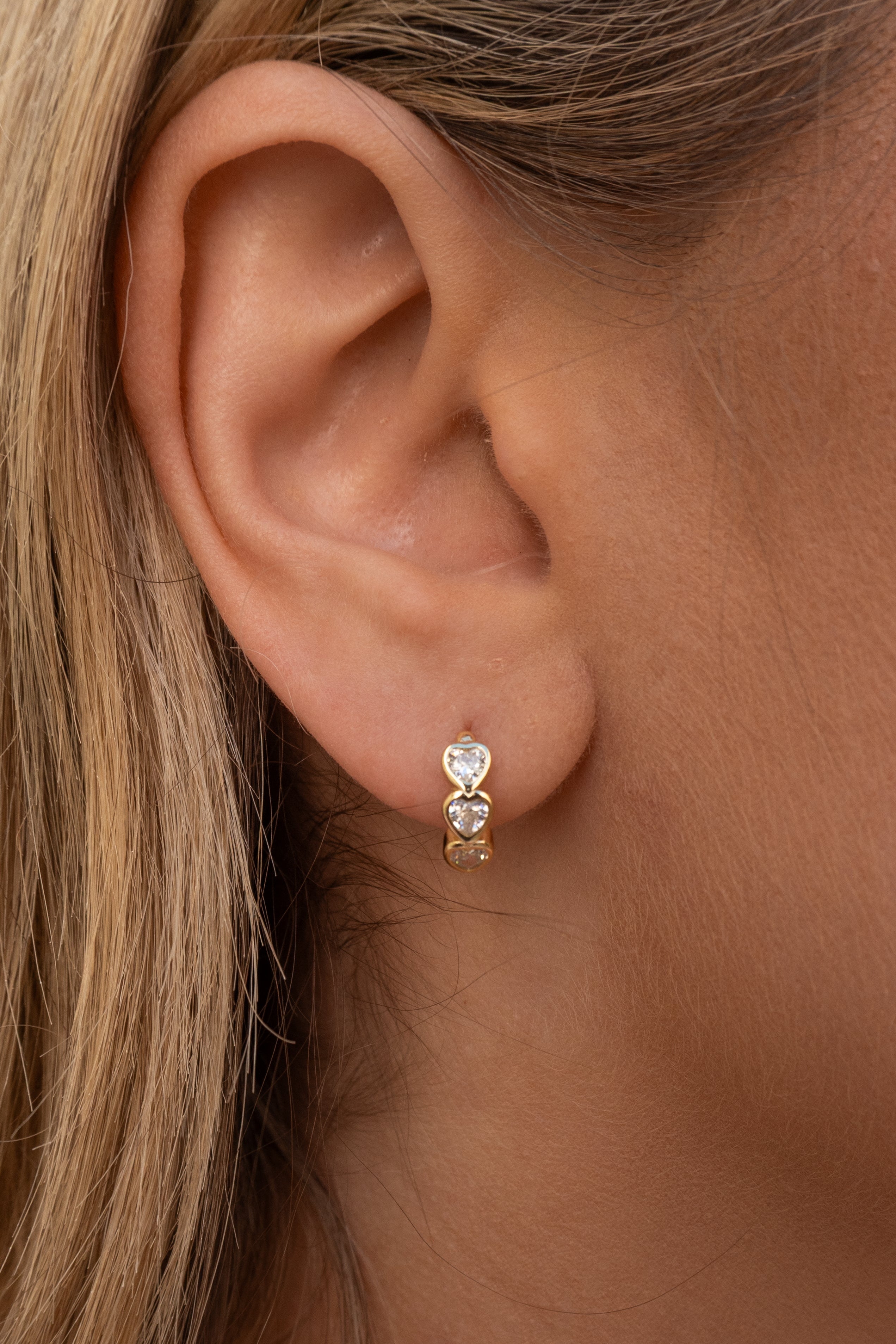 Close-up of an ear wearing a gold hoop earring with a heart-shaped gemstone.