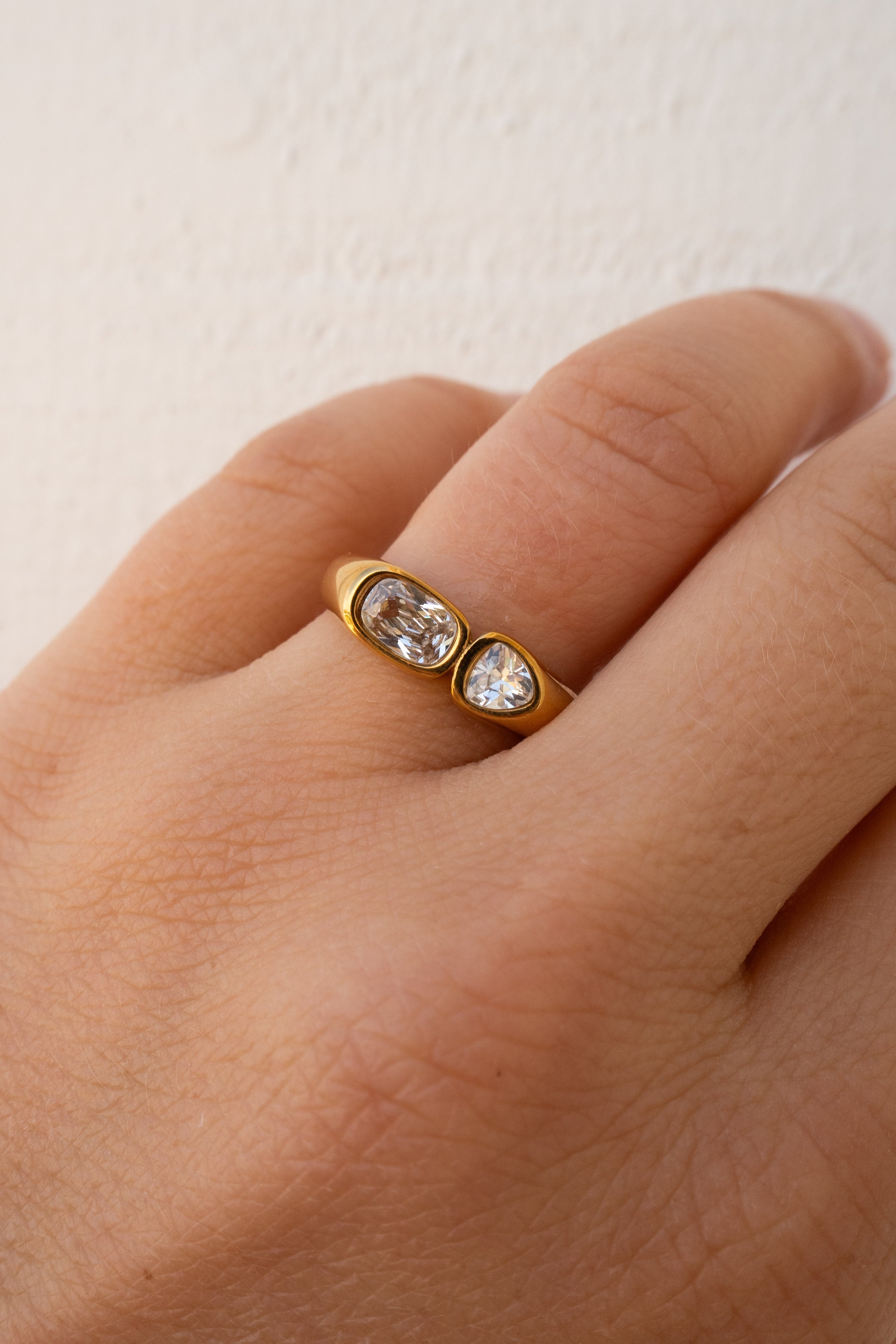 Gold ring with two clear stones on a hand against a light background