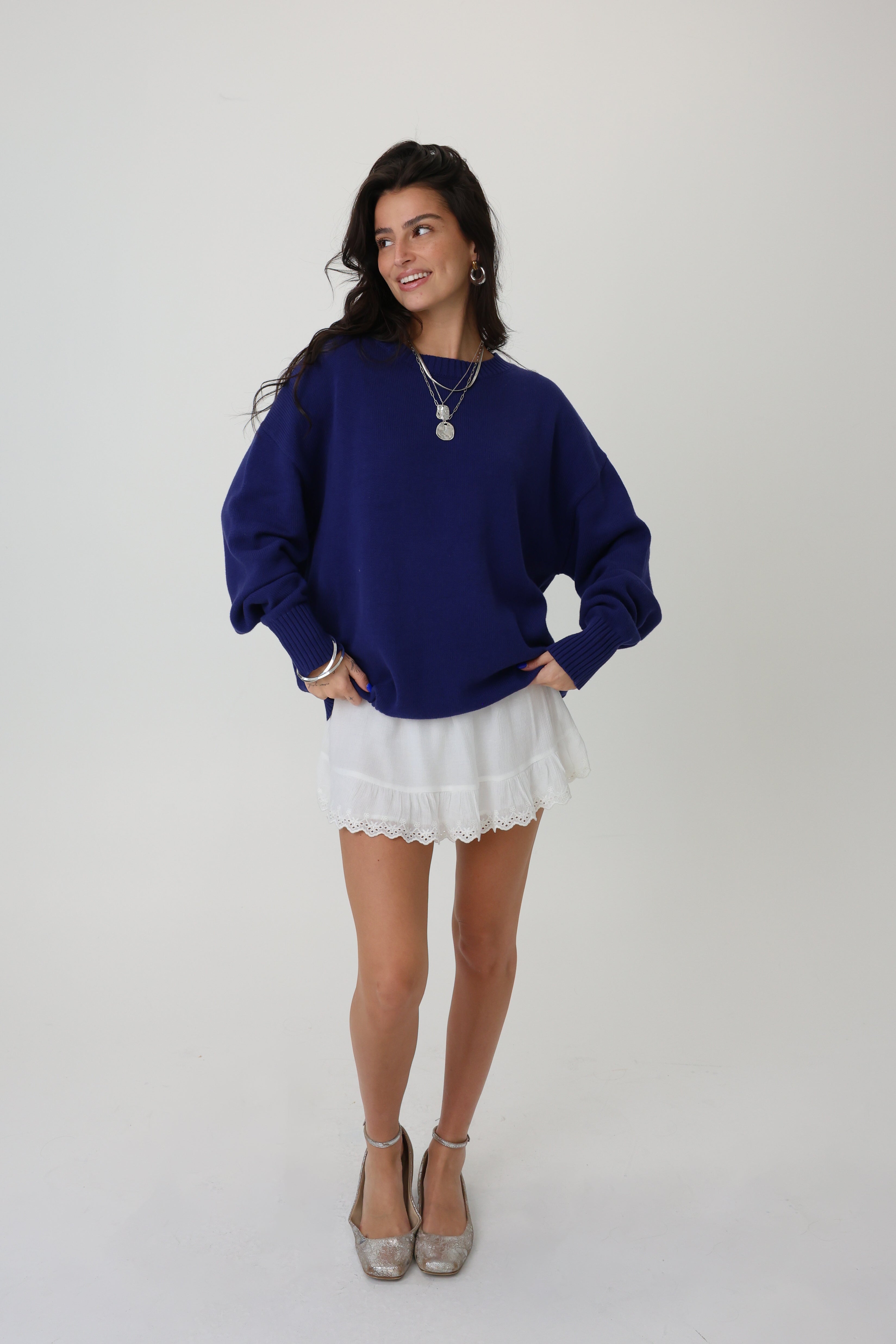 Woman wearing a blue sweater and white skirt on a plain background