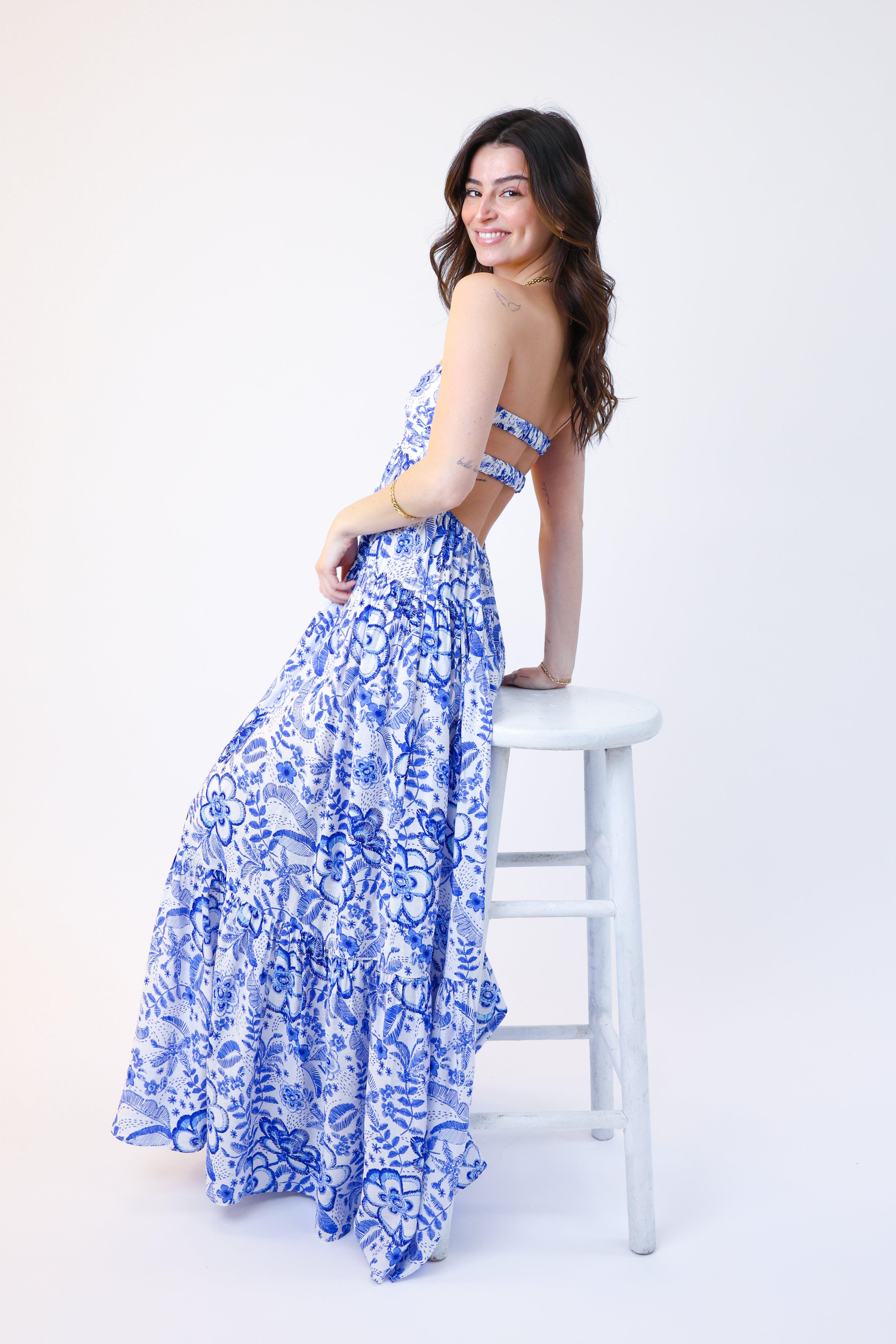 Woman in a blue floral dress sitting on a white stool against a white background