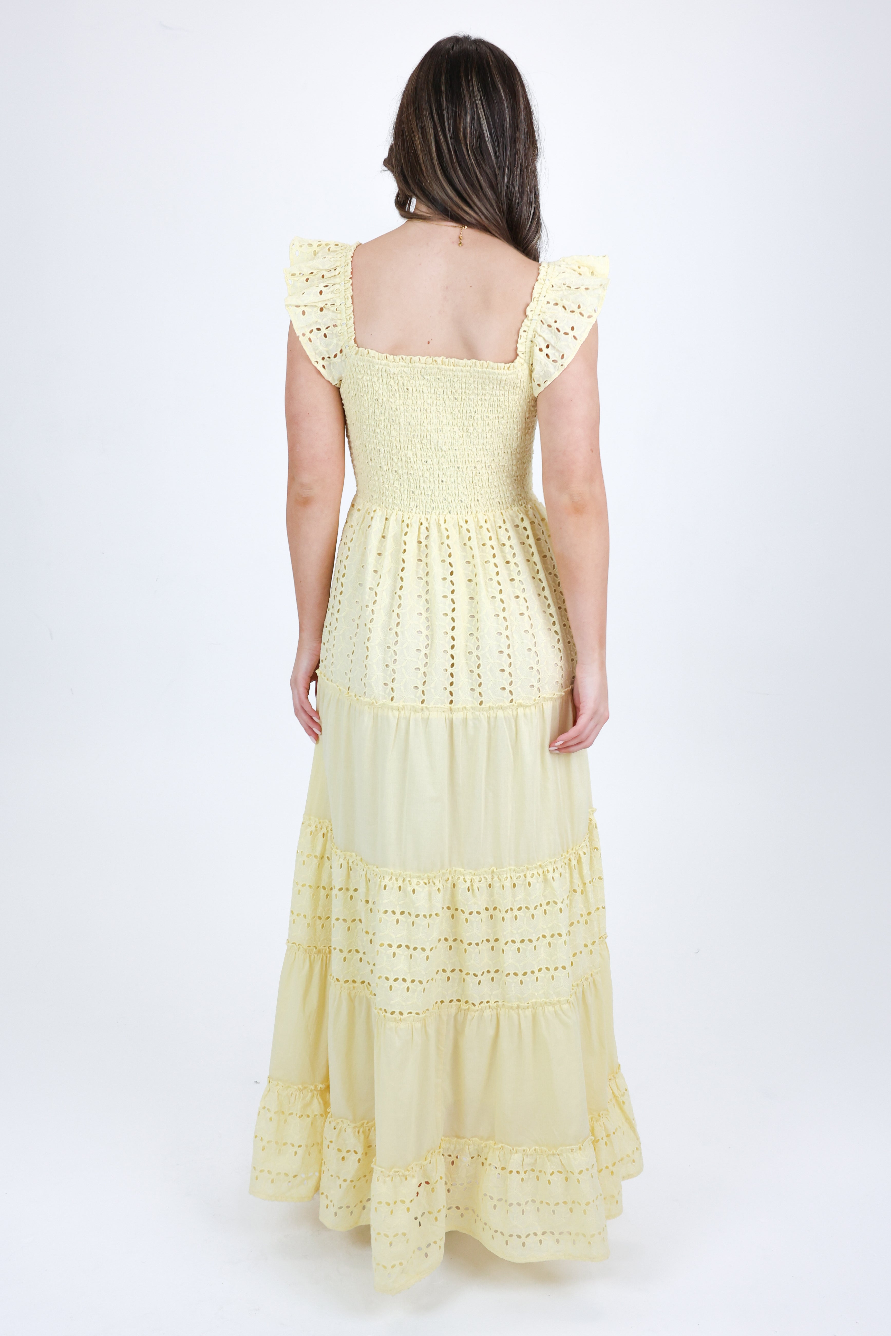 Woman wearing a light yellow dress with lace details on a white background