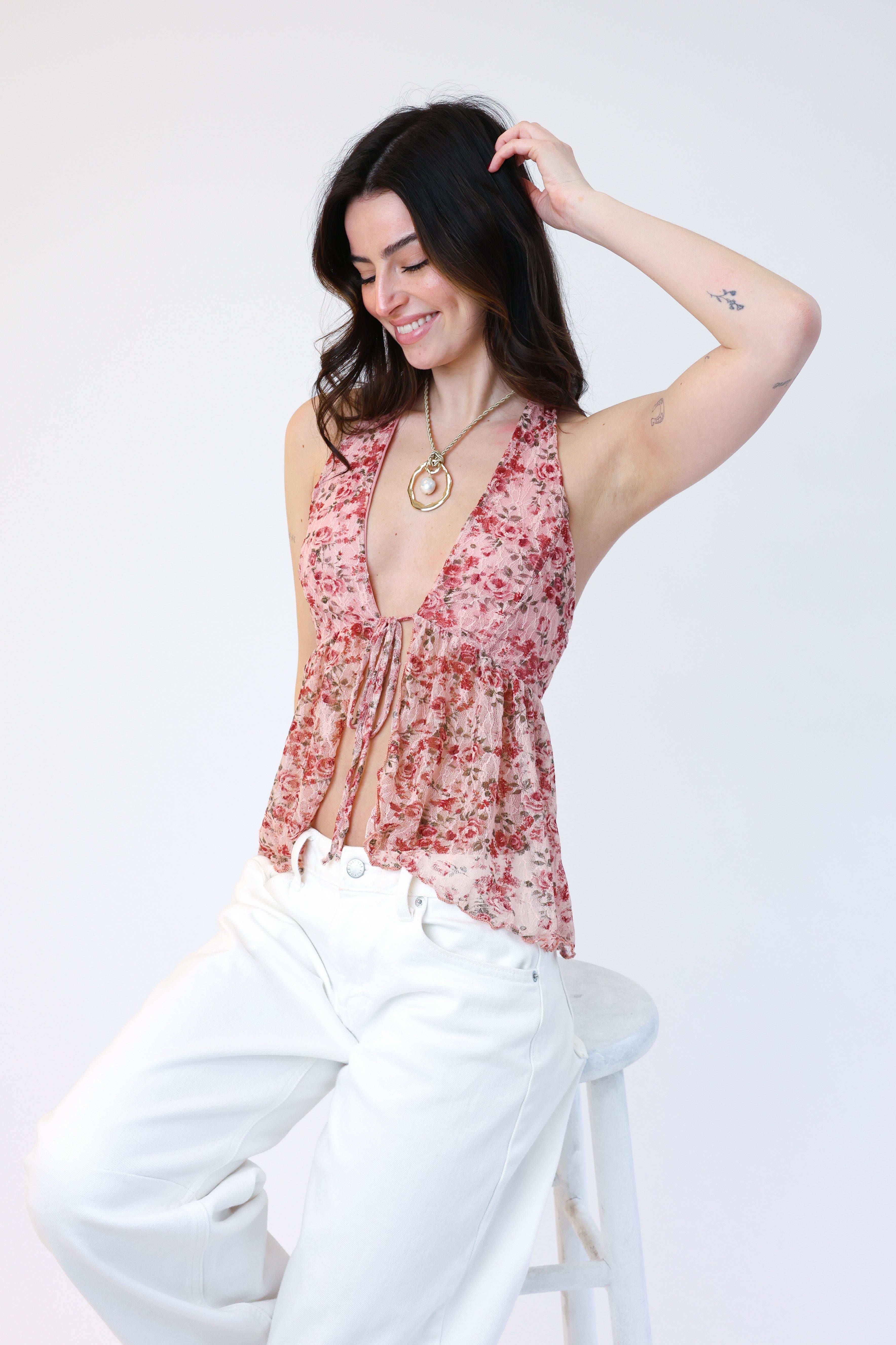 Woman wearing a floral top and white pants against a plain background