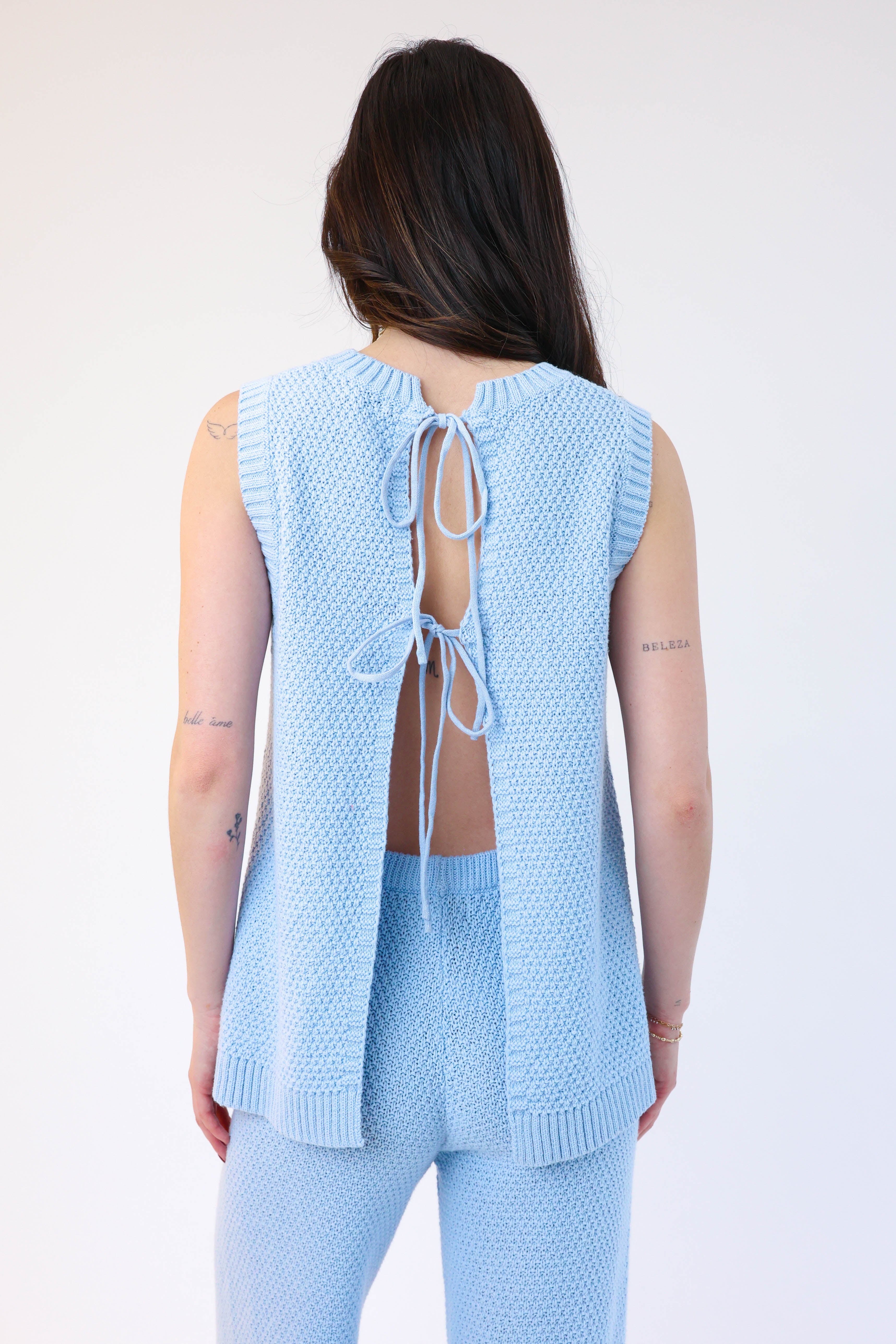 Woman wearing a light blue knit outfit with a backless top on a white background