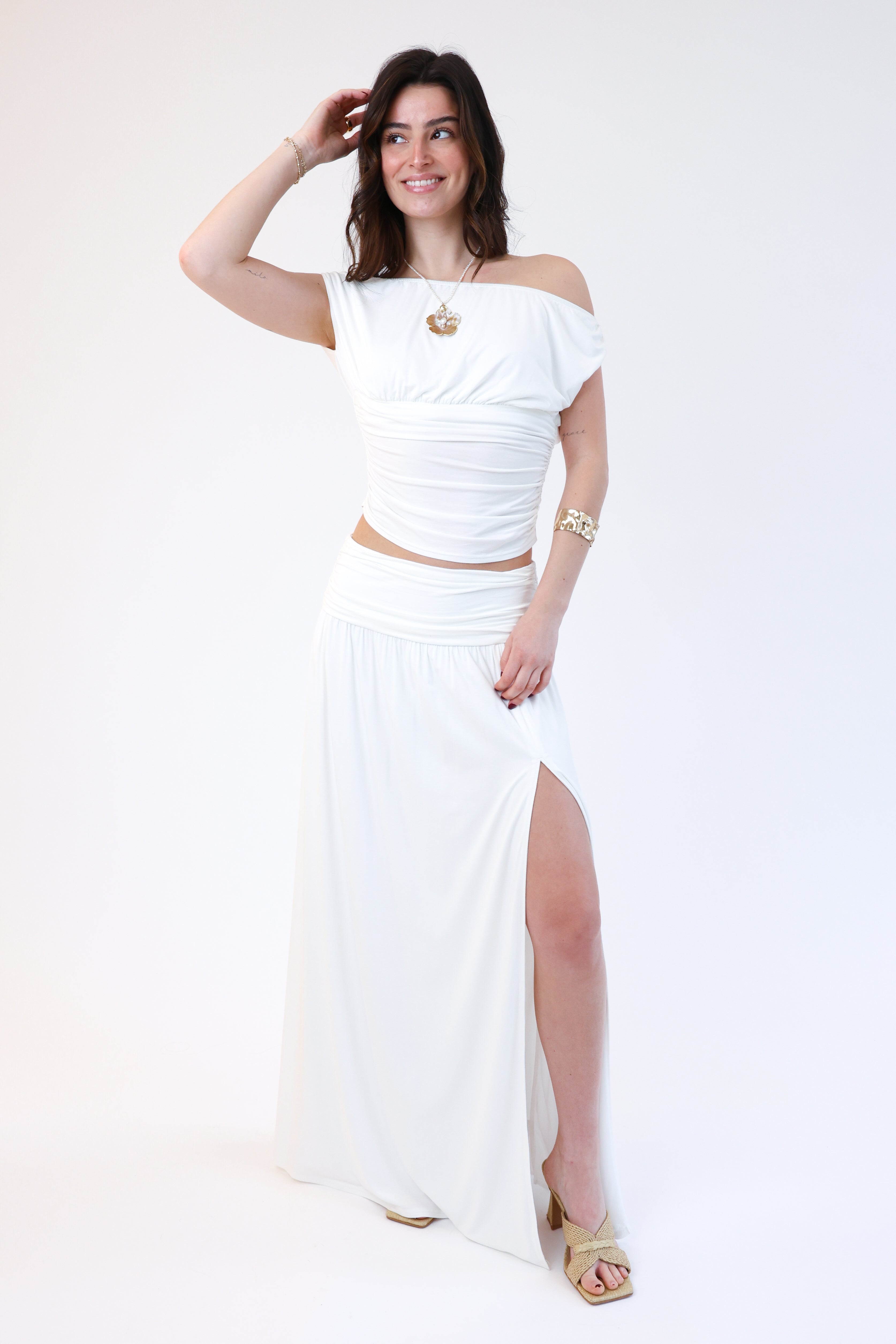 Woman wearing a white off-shoulder top and long skirt with gold accents on a white background
