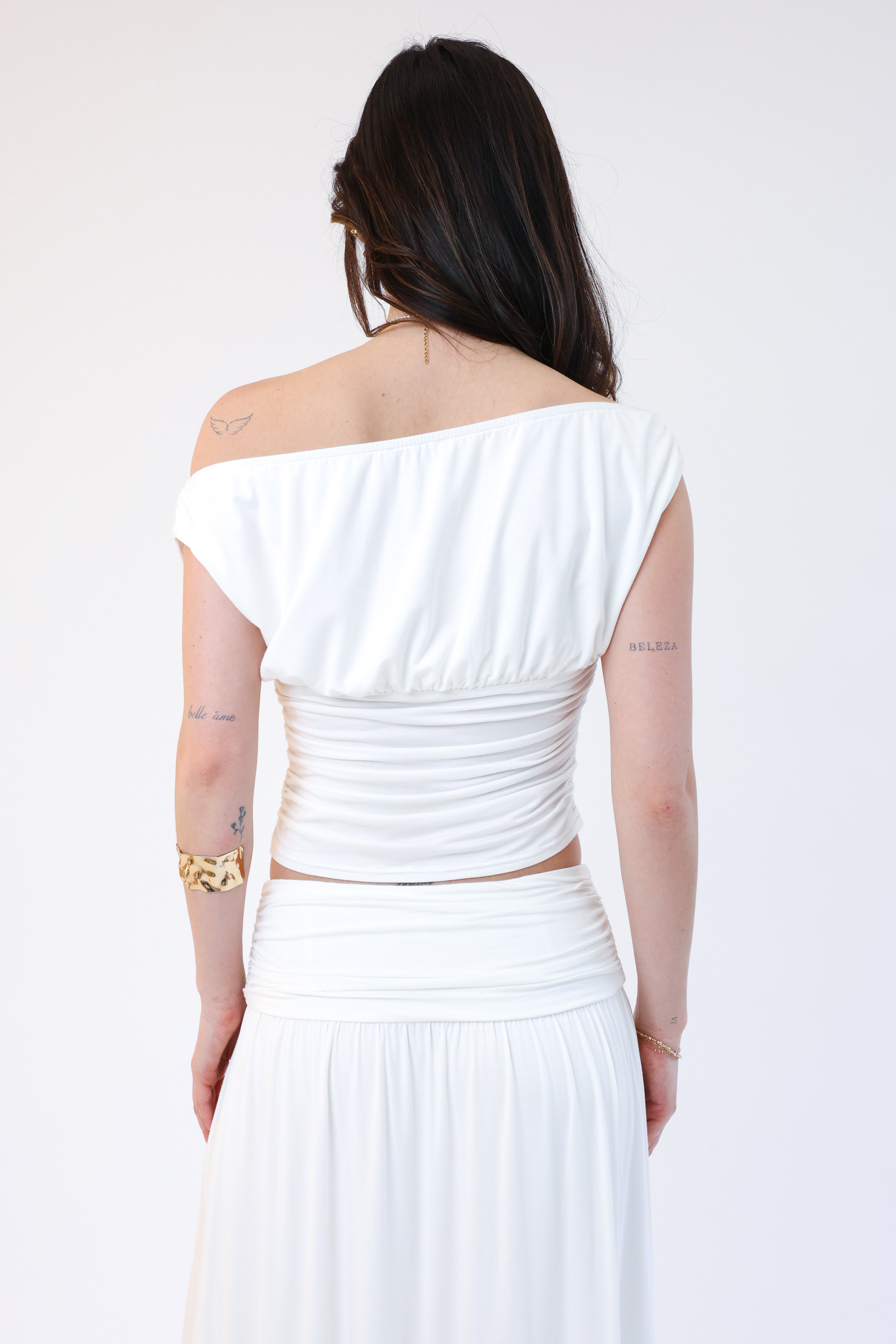 Woman wearing a white off-shoulder top and skirt set on a plain background