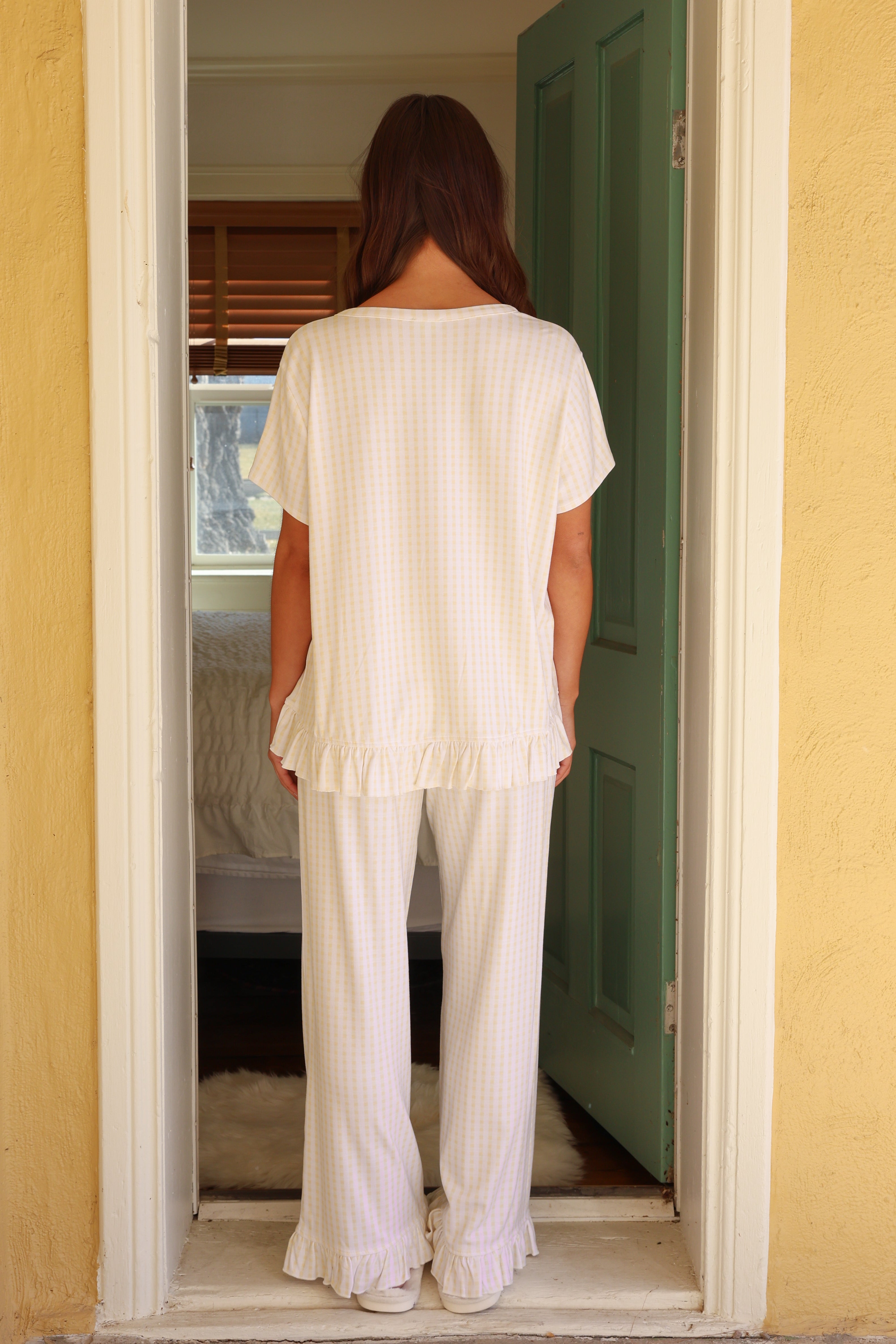 Woman in a white outfit standing in a doorway with a yellow wall and green door.