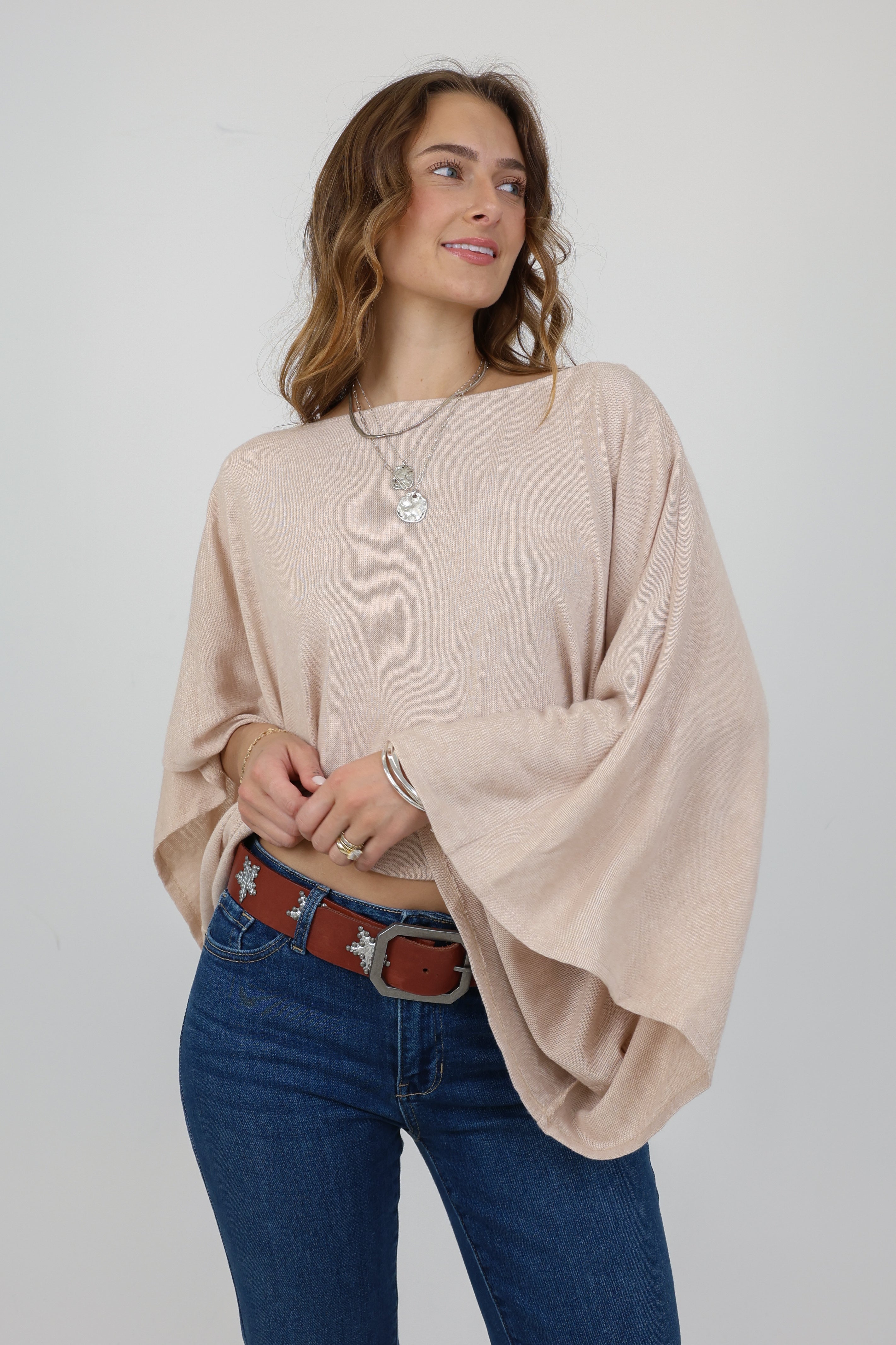 Woman wearing a beige poncho and blue jeans with a white background