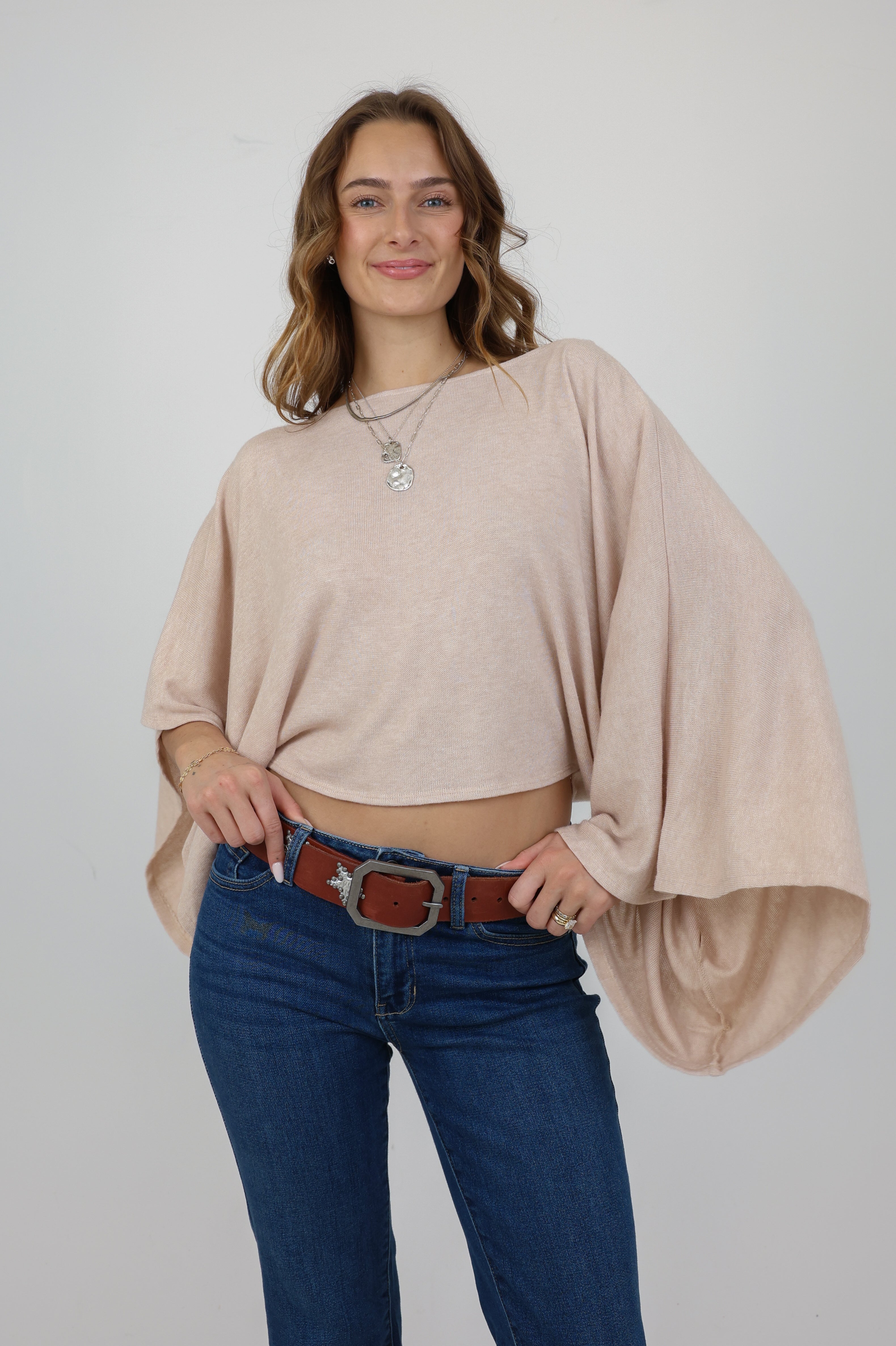 Woman wearing a beige oversized sweater and blue jeans on a plain background