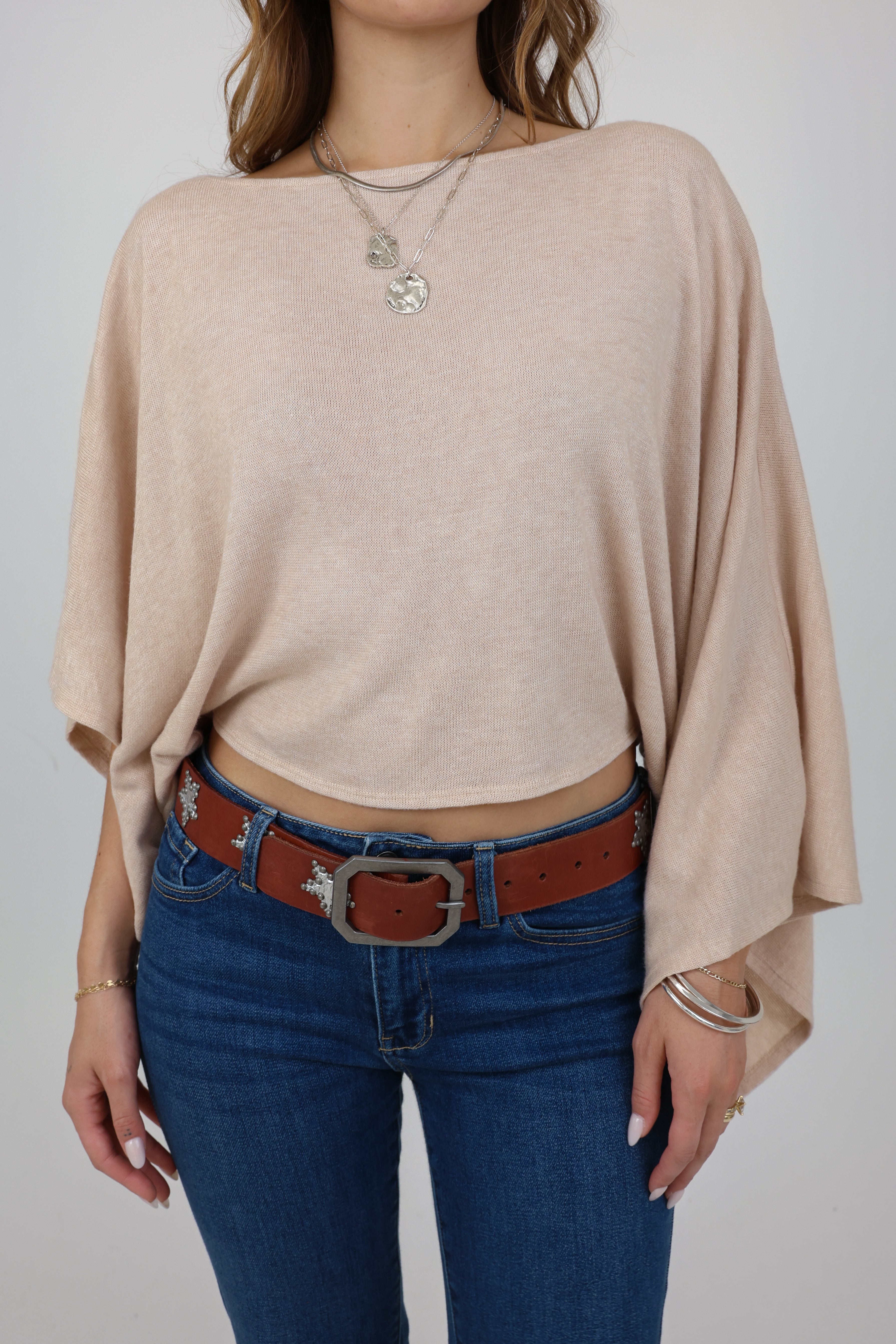 Person wearing a beige sweater and blue jeans with a brown belt on a plain background