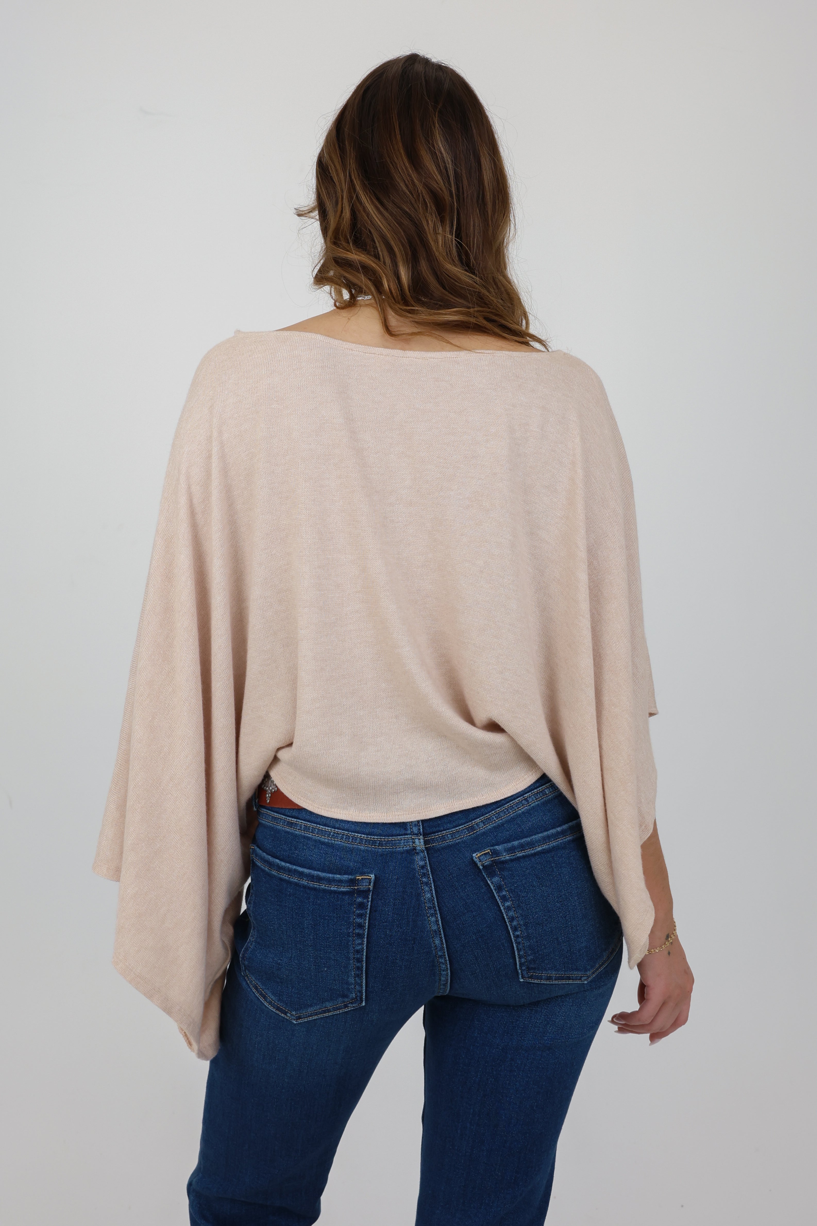 Person wearing a beige sweater and blue jeans on a plain background