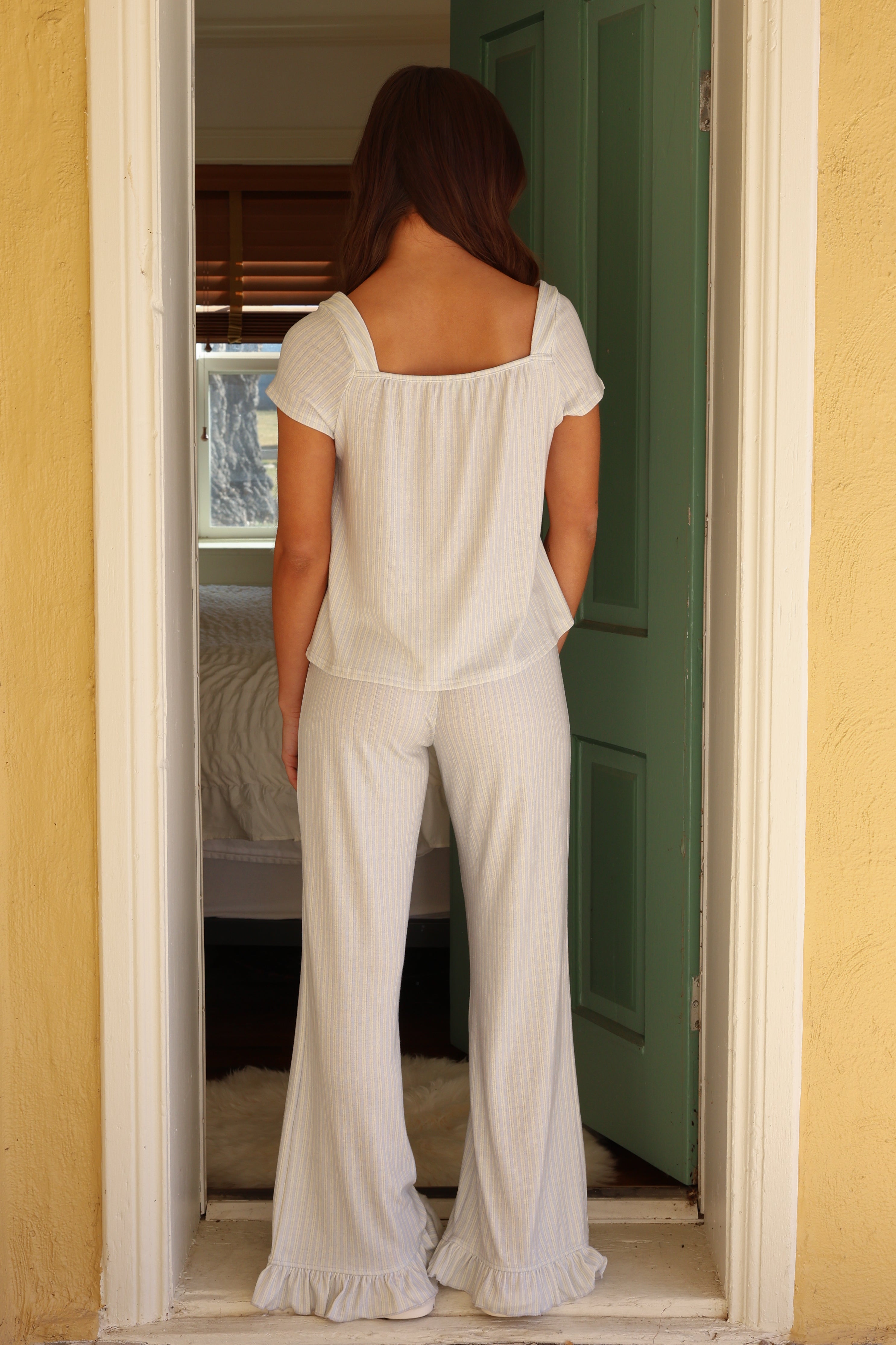 Woman in a white outfit standing in a doorway with a yellow wall and green door.