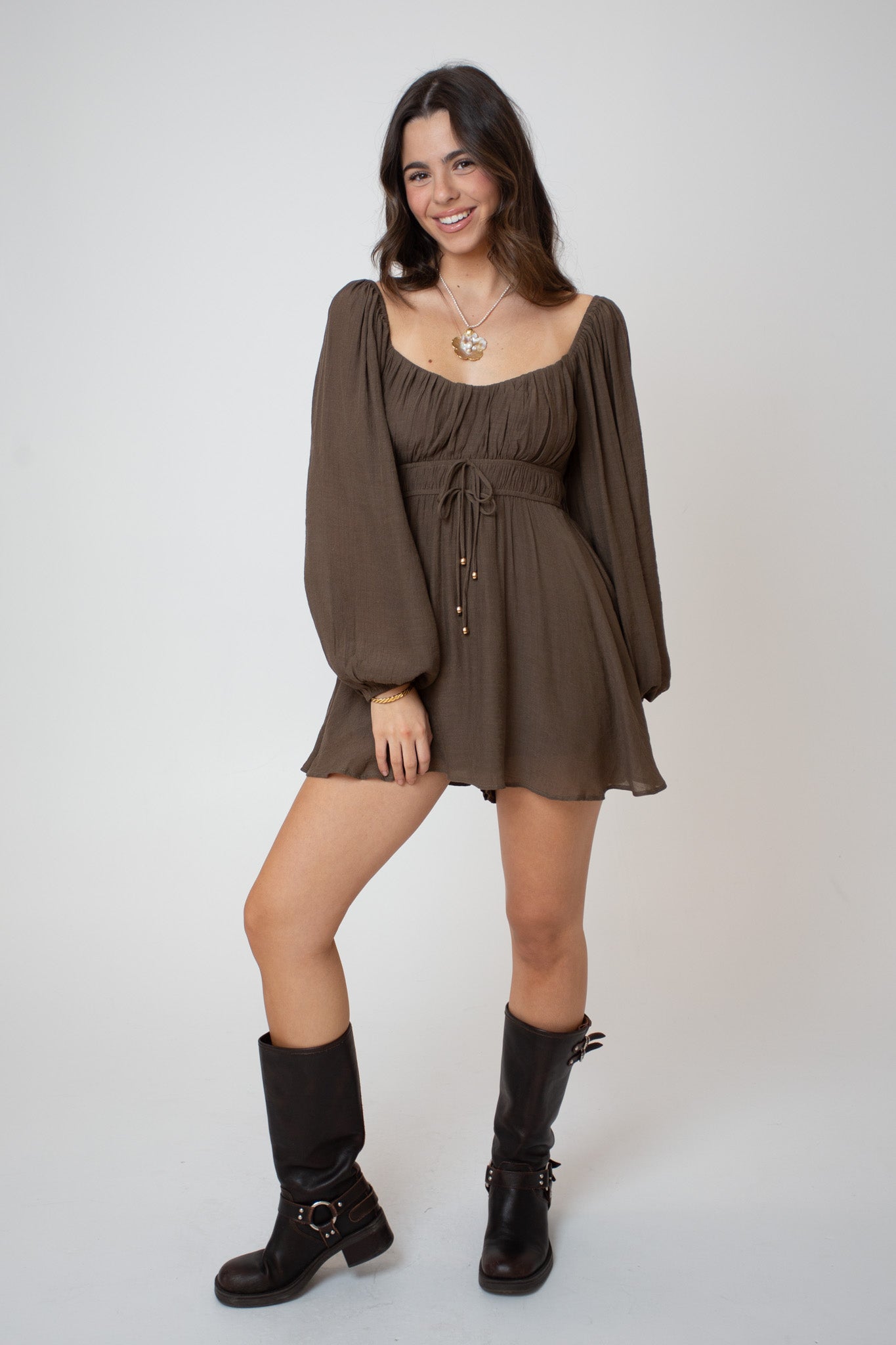 Woman wearing a brown dress with long sleeves and black boots on a white background