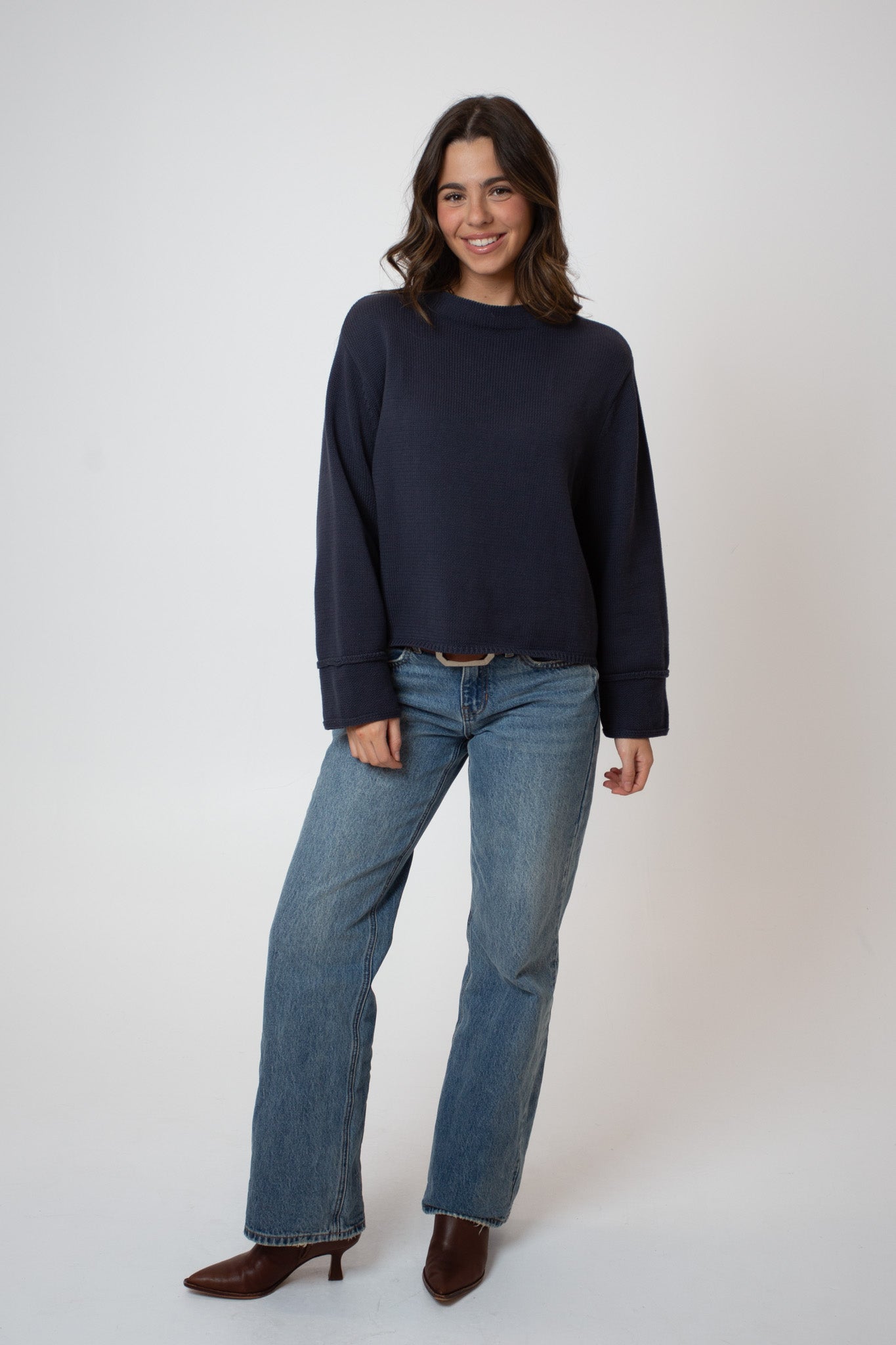 Woman wearing a navy sweater and blue jeans on a white background